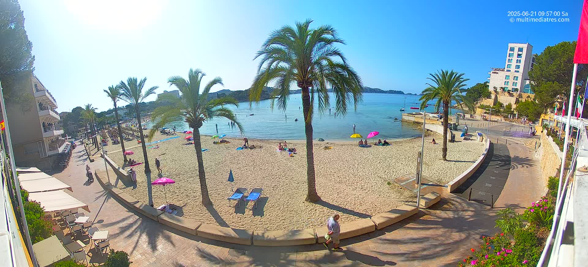 A sunny day at a sandy beach with palm trees, people relaxing, and buildings in the background.