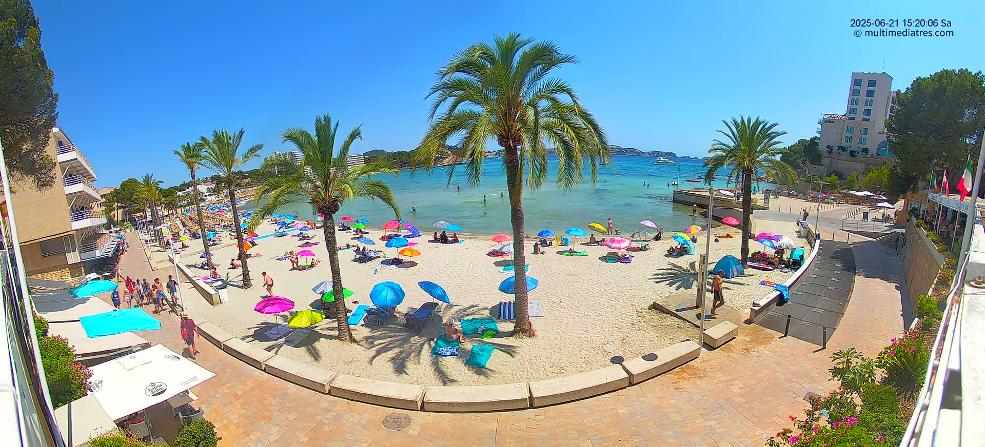 A sandy beach with colorful umbrellas and many people relaxing under a clear blue sky.