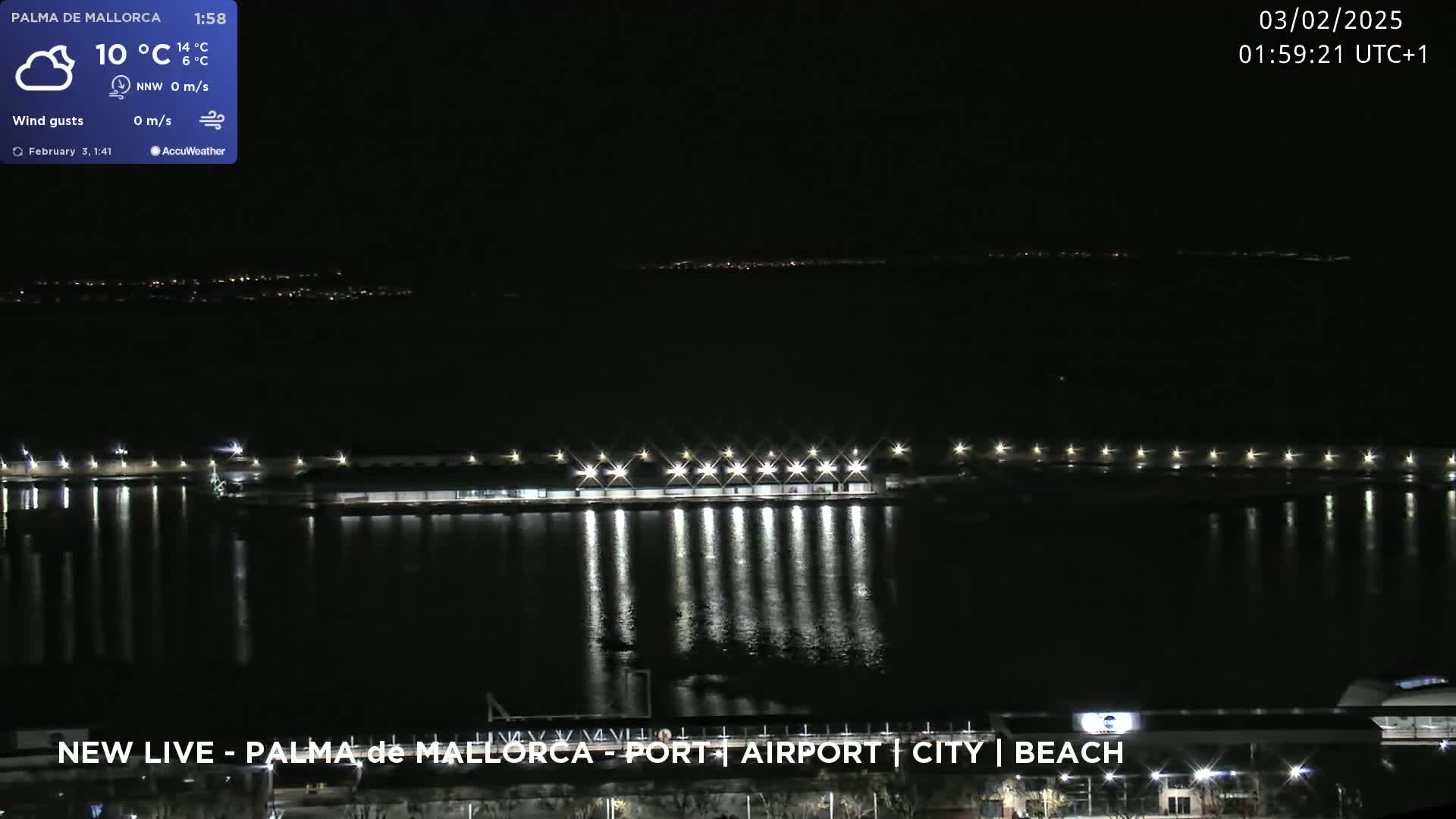 A nighttime view of a brightly lit harbor and city skyline reflected in calm water under a clear sky.