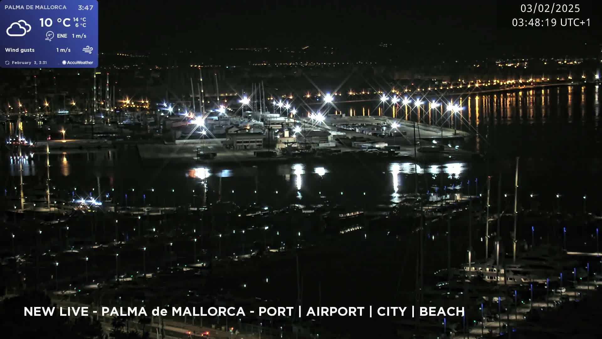 A nighttime aerial view of a harbor filled with boats, illuminated by lights, with a calm body of water reflecting the city lights in the background.
