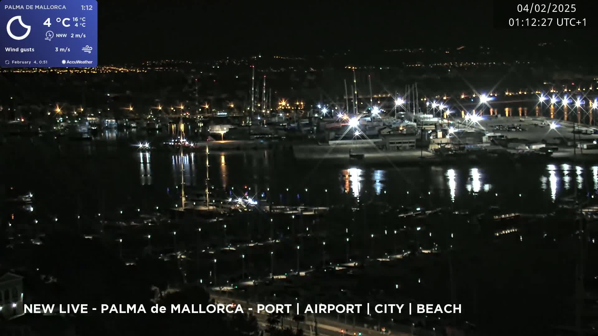 A nighttime aerial view of a harbor filled with boats, illuminated by lights, under a clear sky.