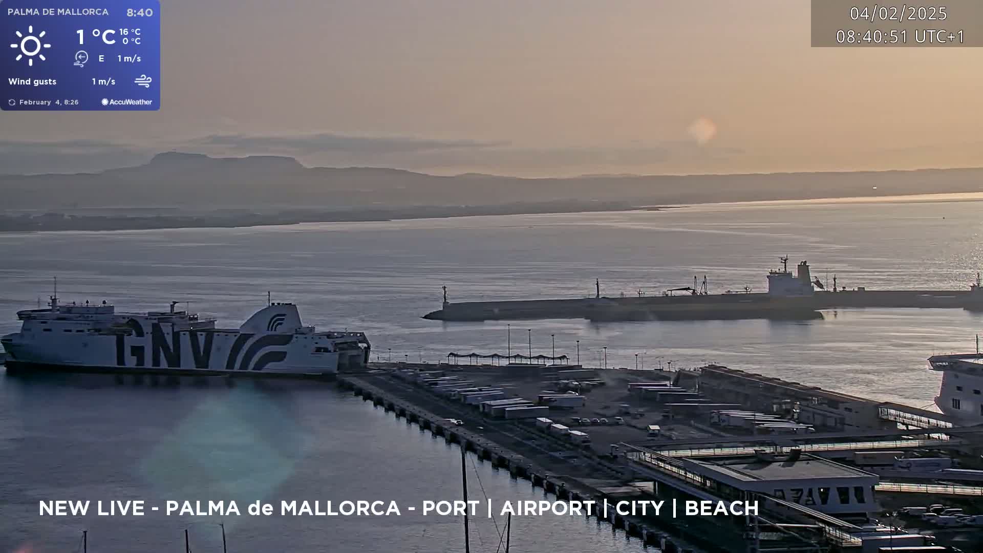 A ferry is docked at a port under a hazy sunrise, with calm water and distant mountains visible.