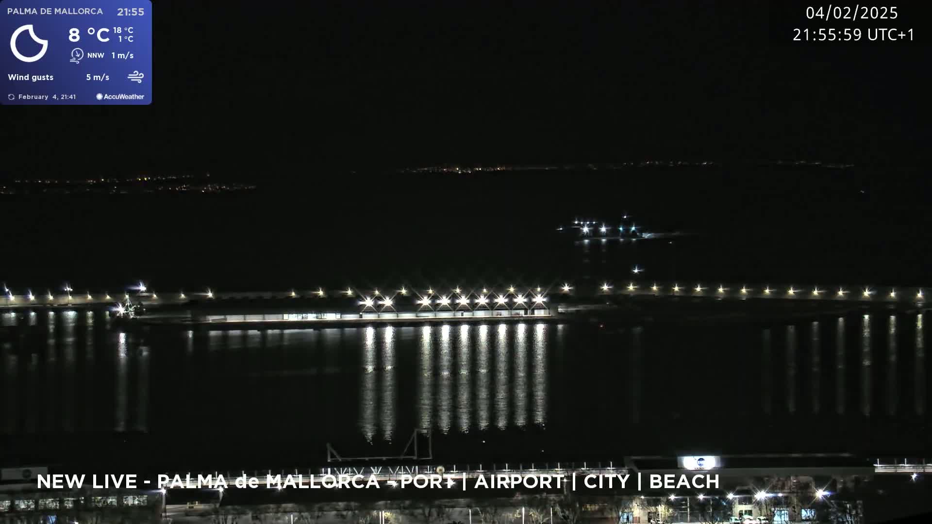 A nighttime view of a brightly lit waterfront area, with calm water reflecting the lights, under a clear, dark sky.