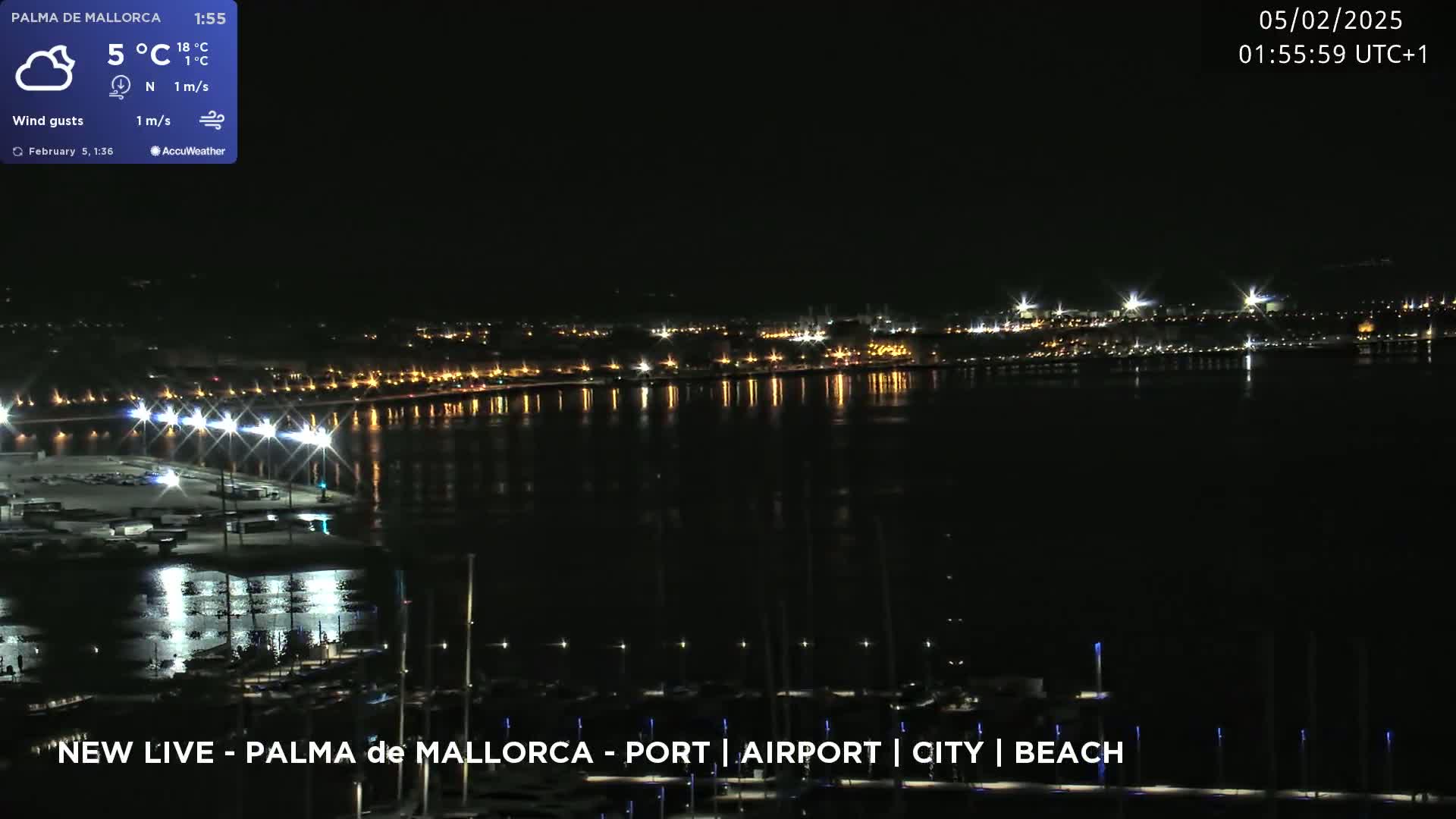A nighttime view of a city's waterfront, showing a harbor with boats and lights reflecting on calm water under a clear, dark sky.