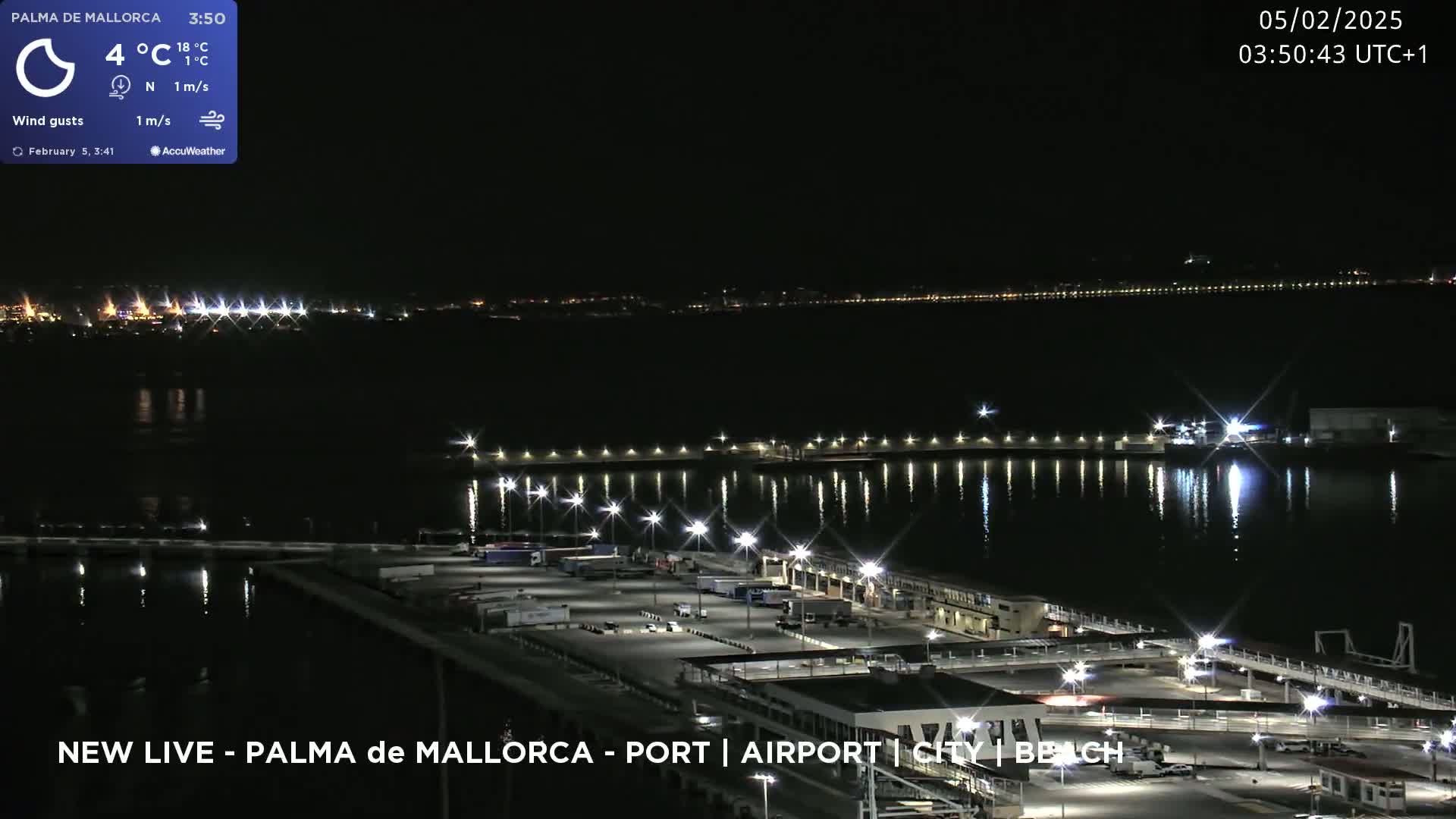 A nighttime view of a harbor with a calm body of water reflecting the lights of the port and distant city, under a clear sky.