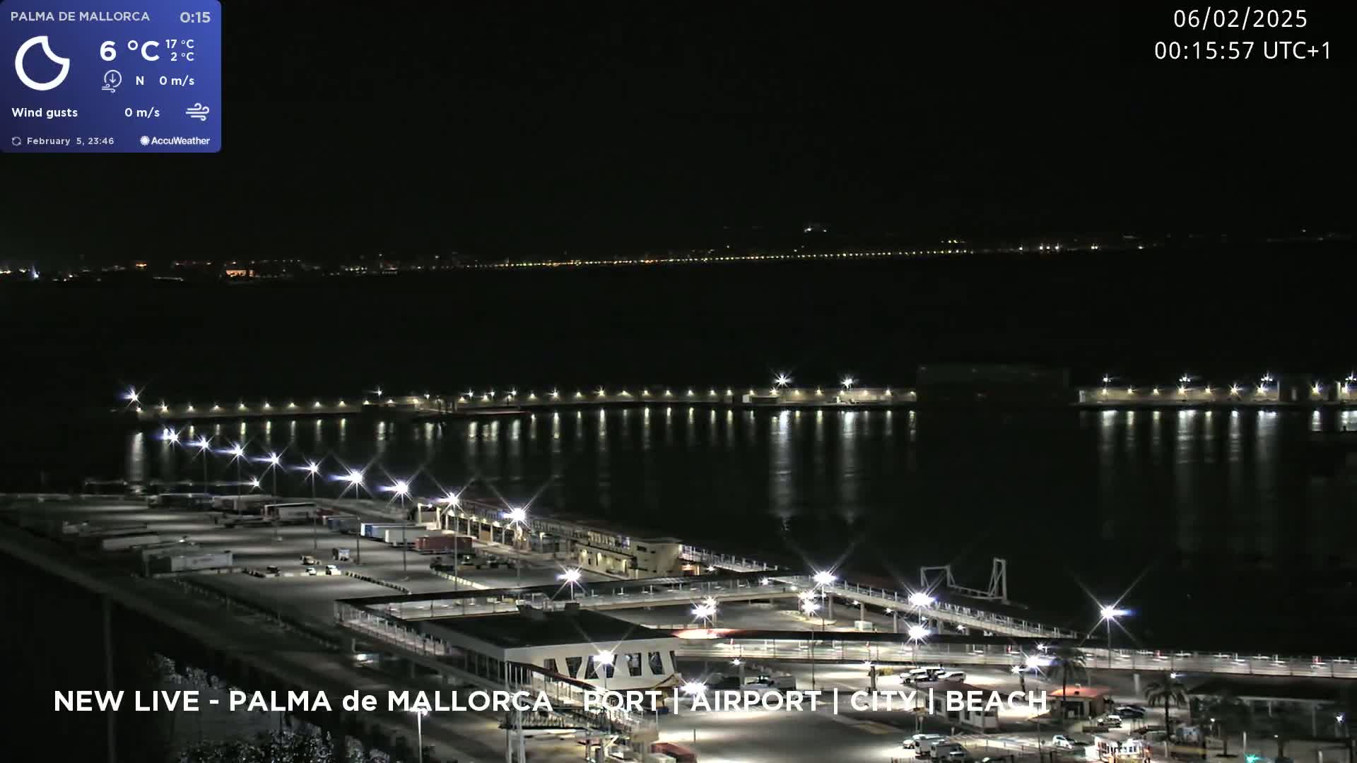 A nighttime aerial view of a port and city, with calm waters reflecting the lights.