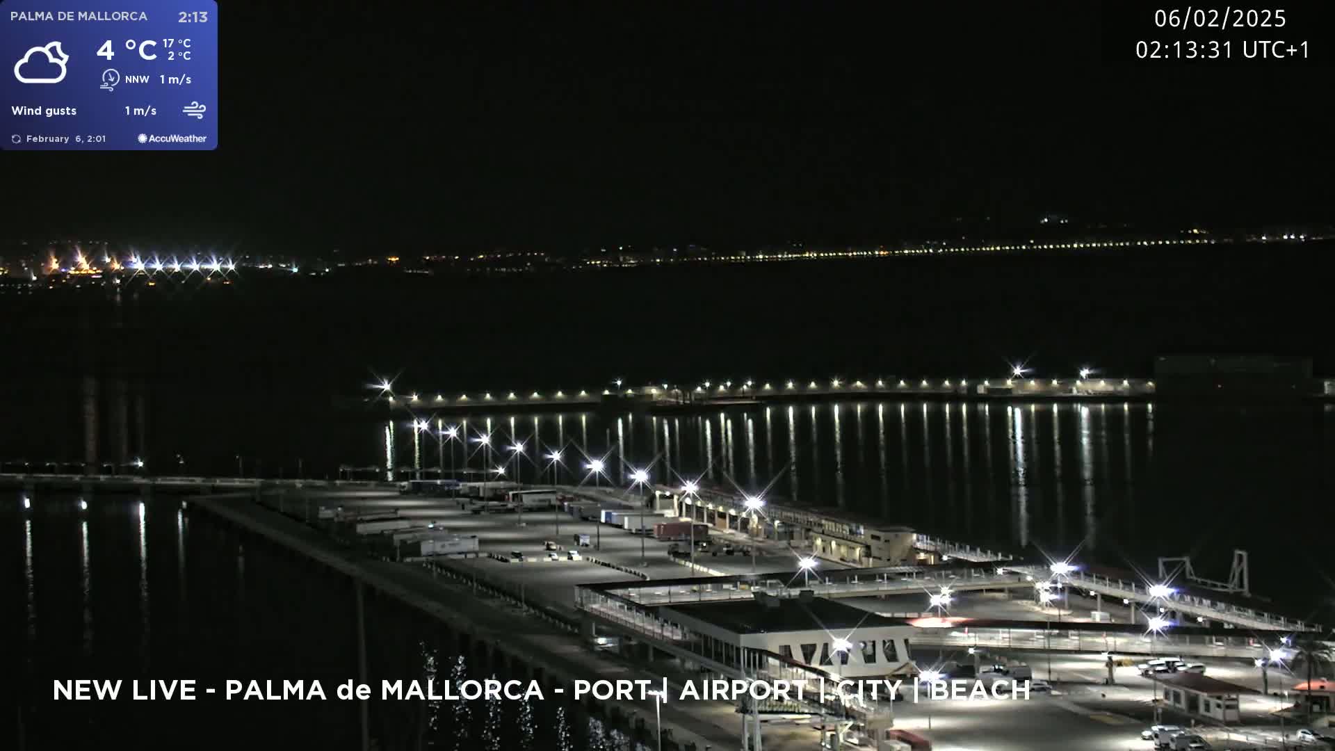 A nighttime, slightly cloudy view of a port area with a calm body of water reflecting city lights.