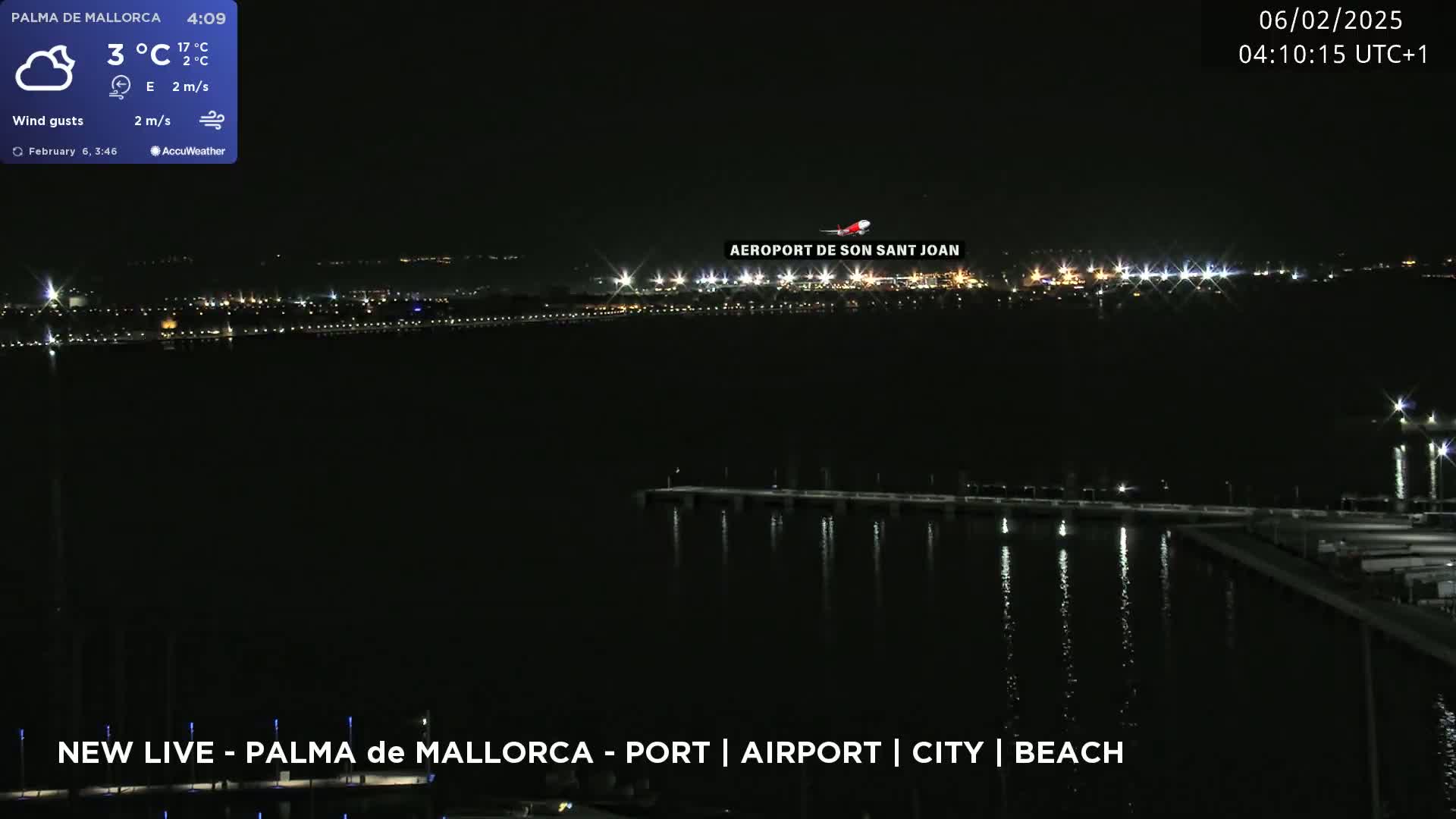 A nighttime view of a city skyline across a dark body of water, with an airplane flying overhead and a calm, windy atmosphere at 3°C.