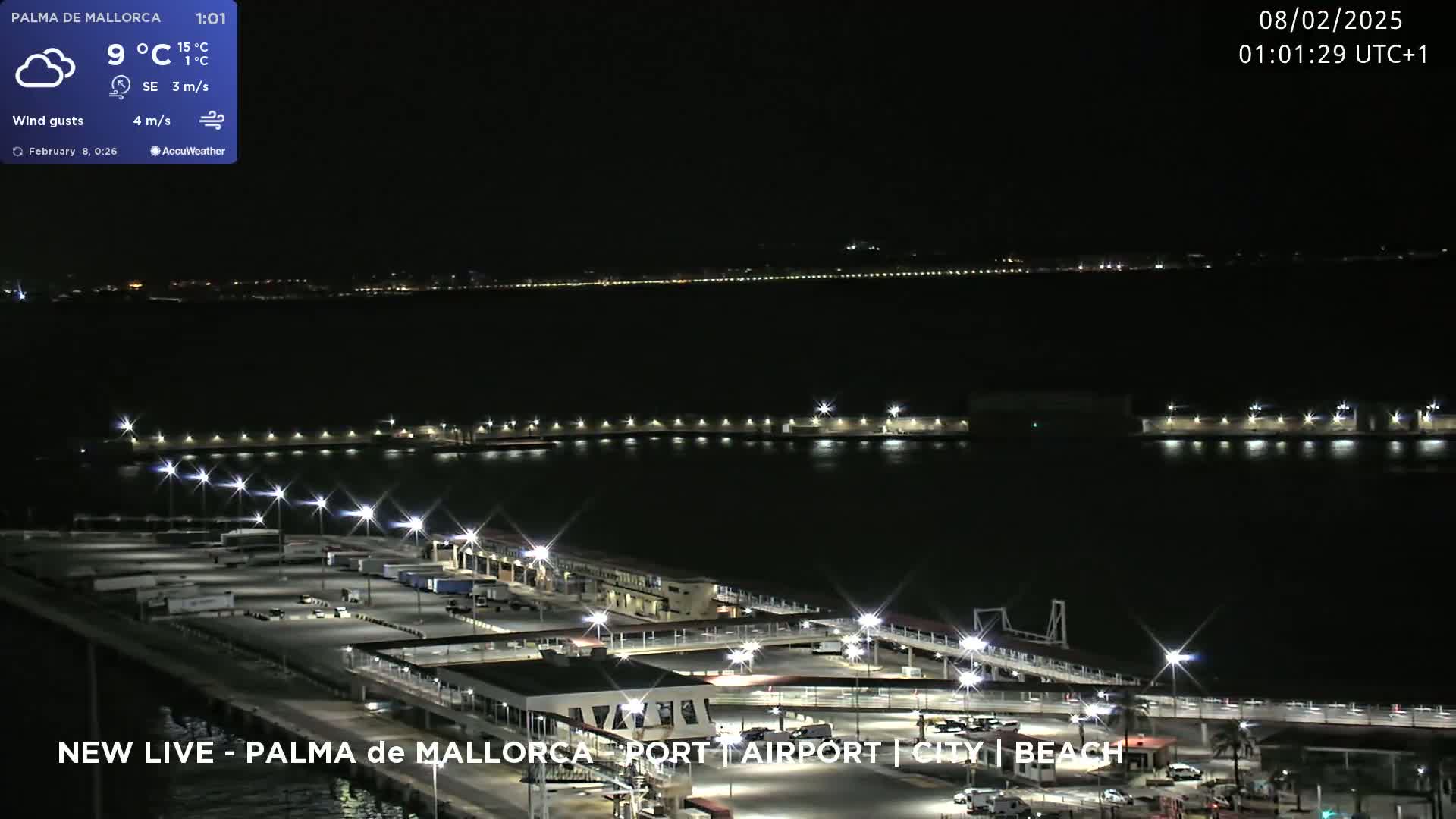 A nighttime, partly cloudy view of a port area with numerous lights illuminating the docks and surrounding land, a body of dark water visible beyond.