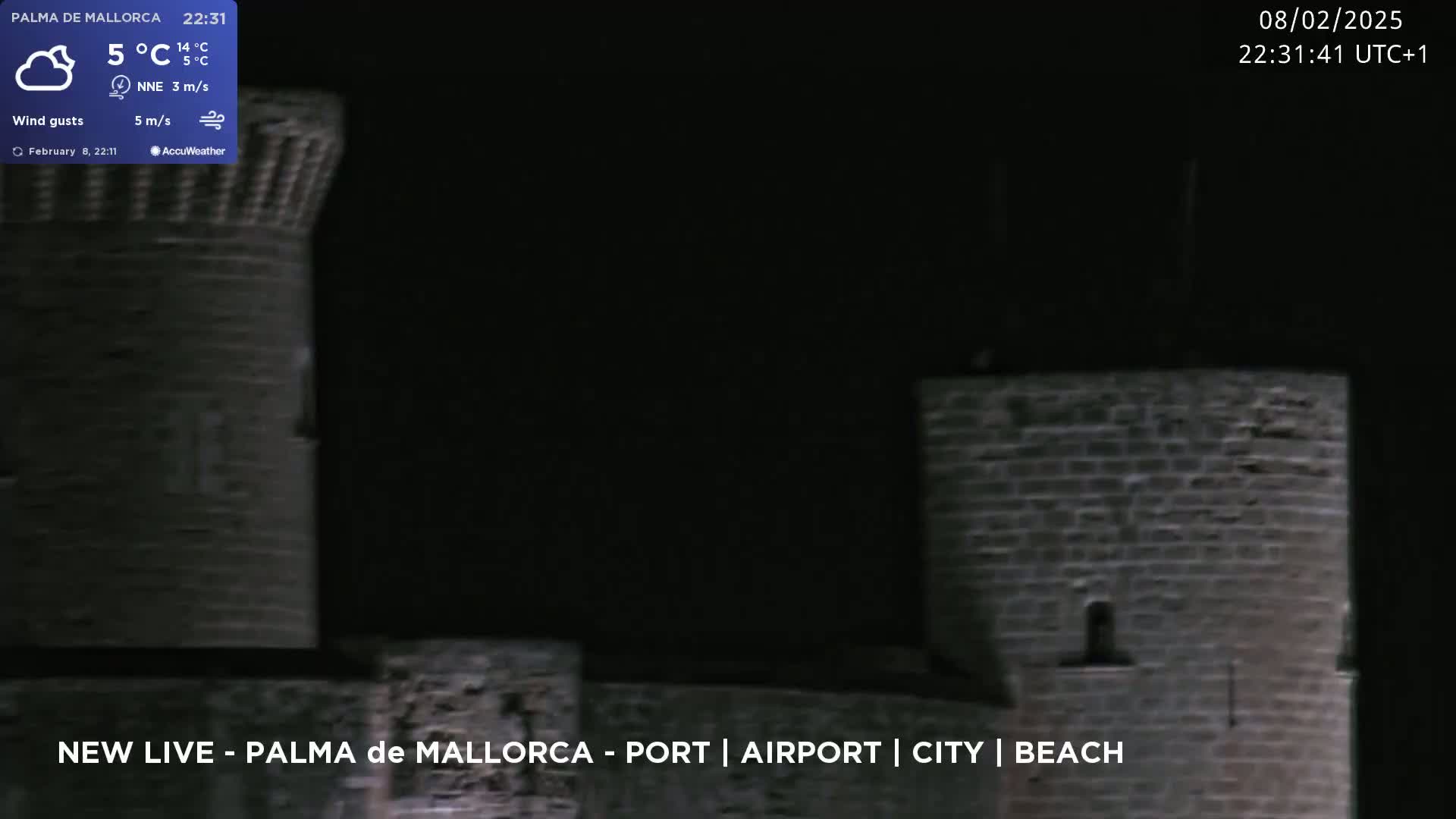 A nighttime view of stone castle walls under a cloudy sky.