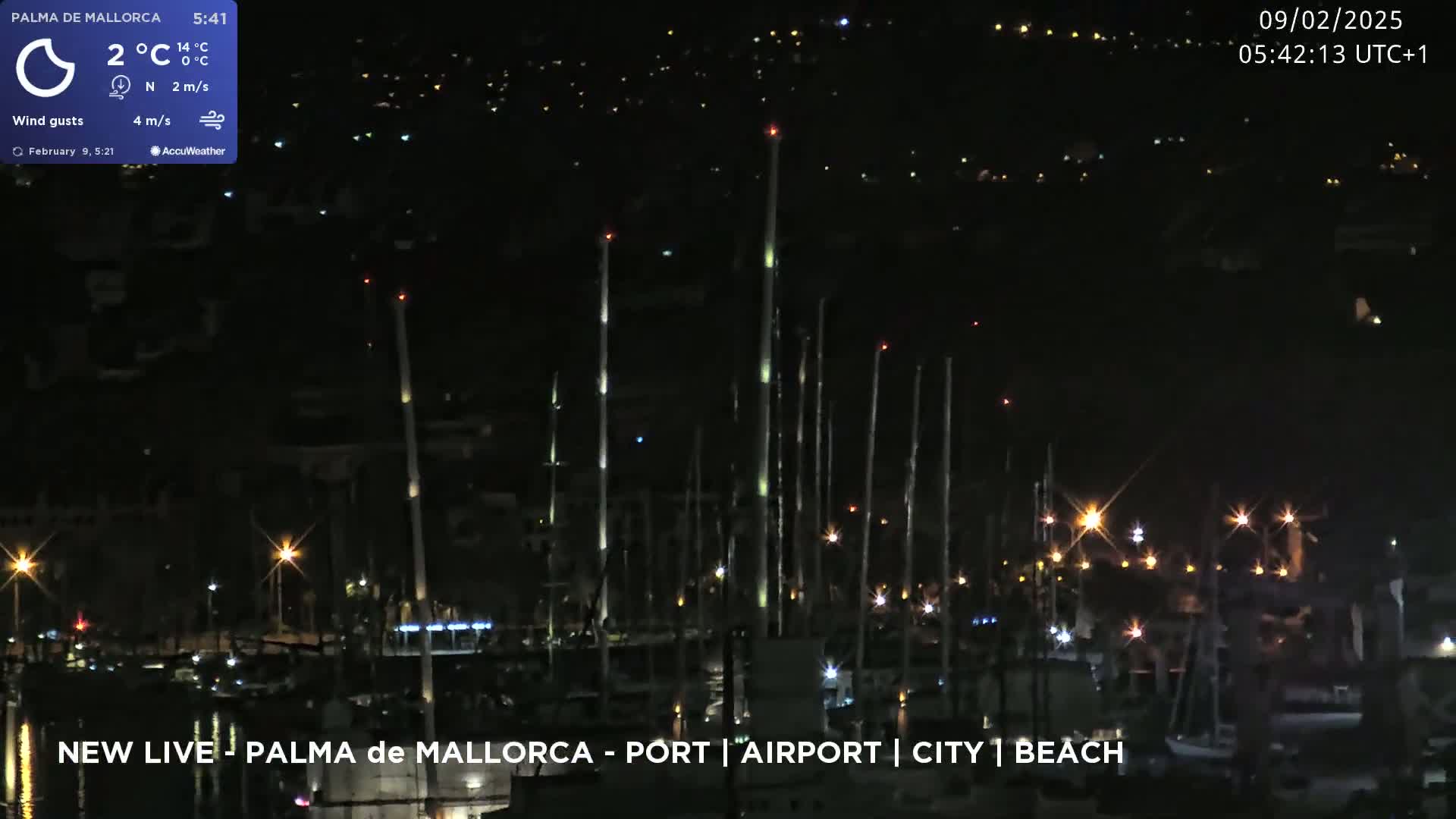 A nighttime view of a harbor filled with boats, illuminated by mast lights and shore lights, under a clear, dark sky.