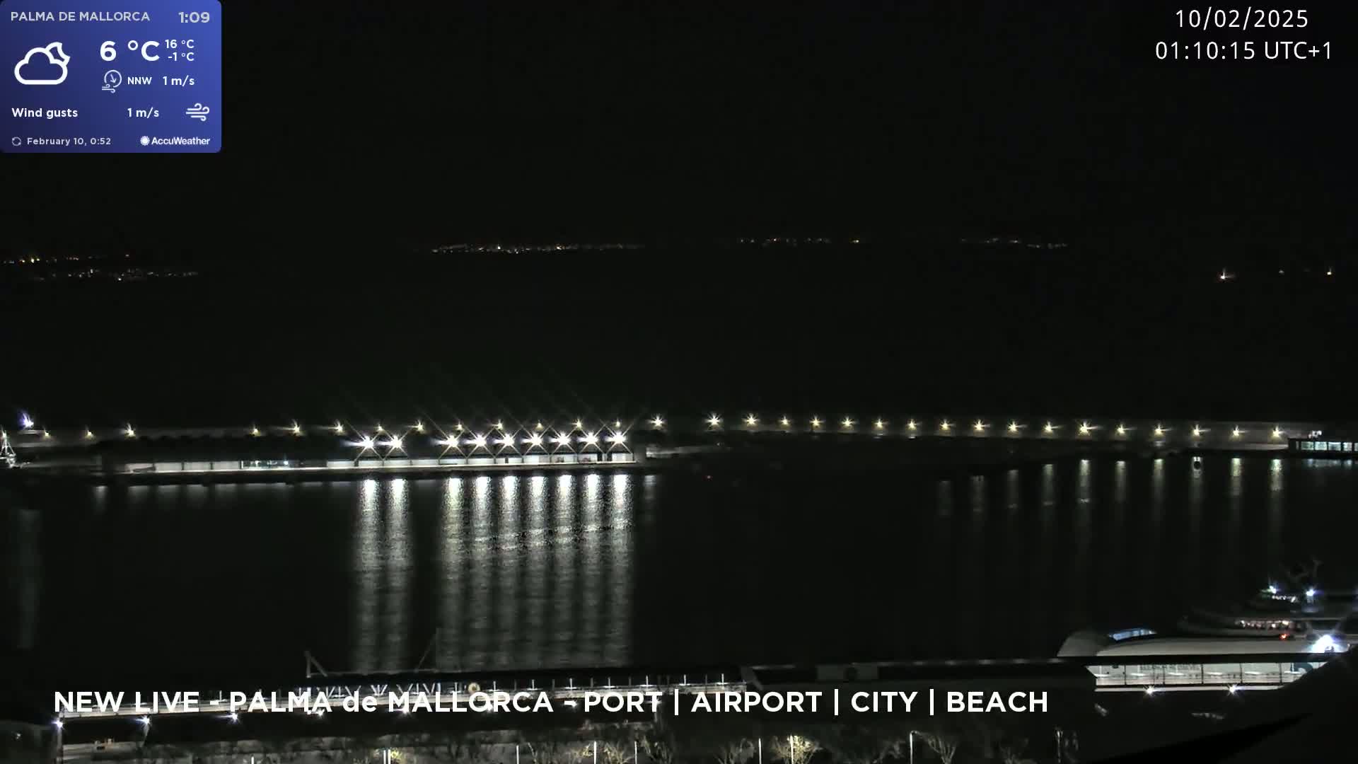 A nighttime view of a brightly lit harbor with calm water reflecting the lights, under a partly cloudy sky.