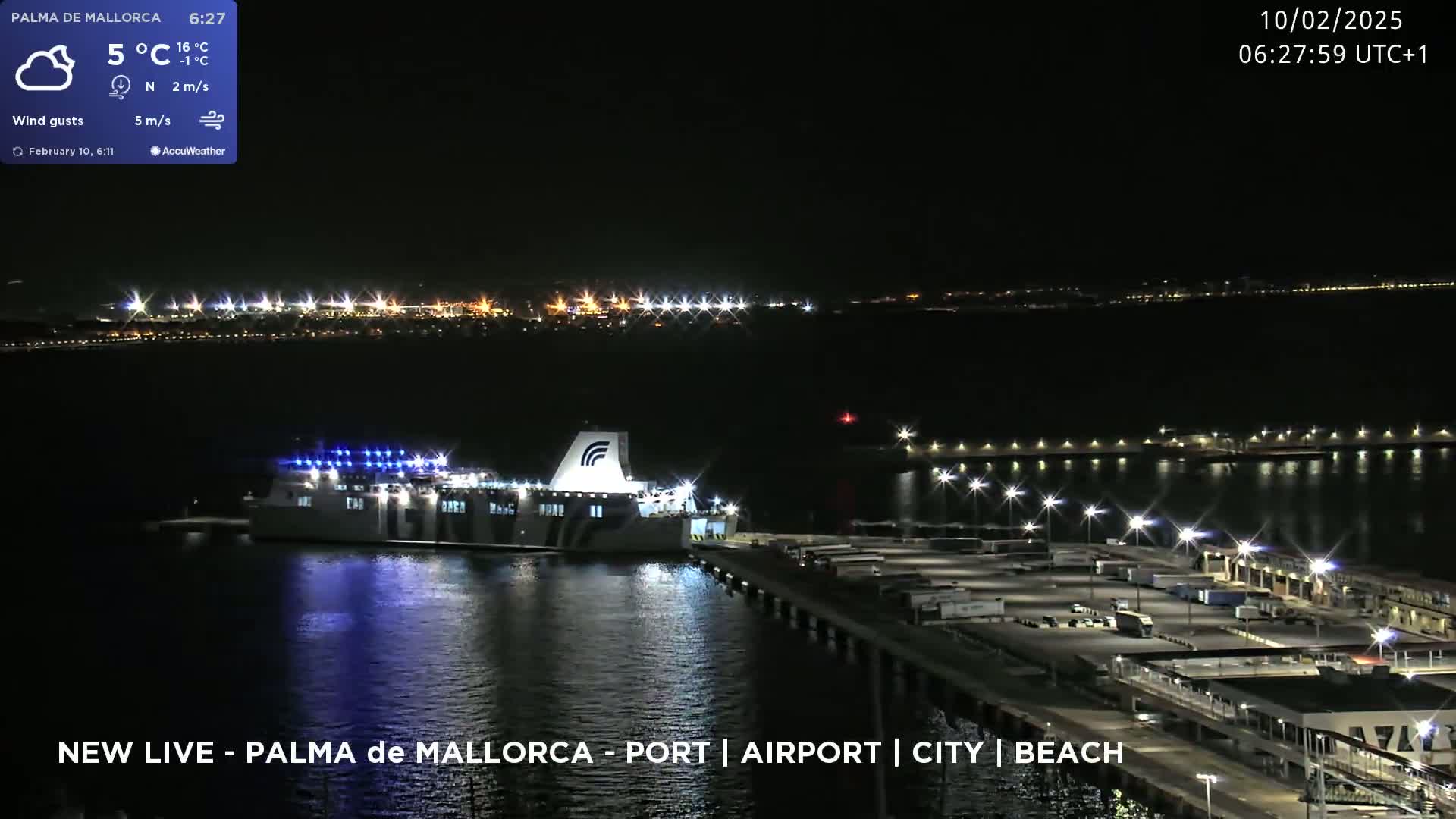A large ferry is docked at a brightly lit port at night, under a partly cloudy sky.