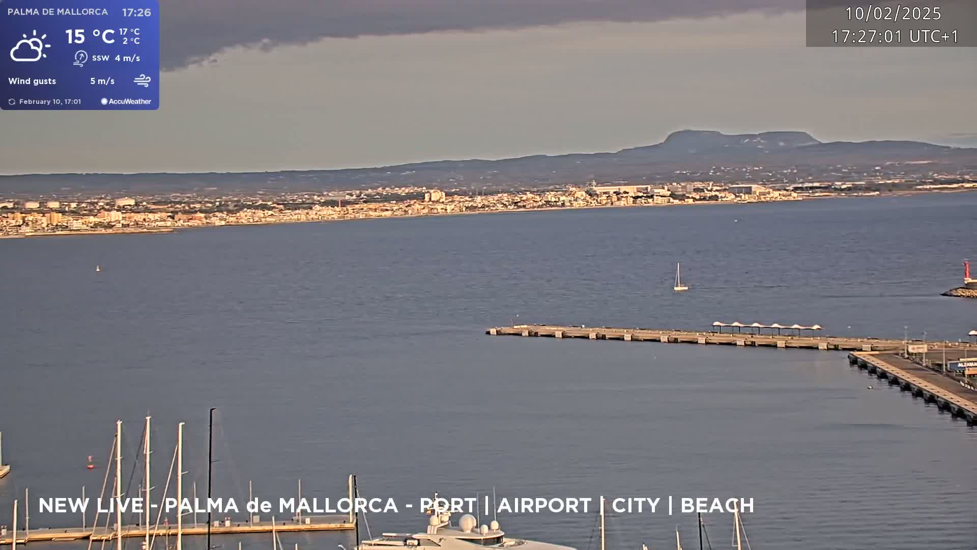 A mostly cloudy day shows a harbor with docked boats and a city across a body of water under a partly cloudy sky.