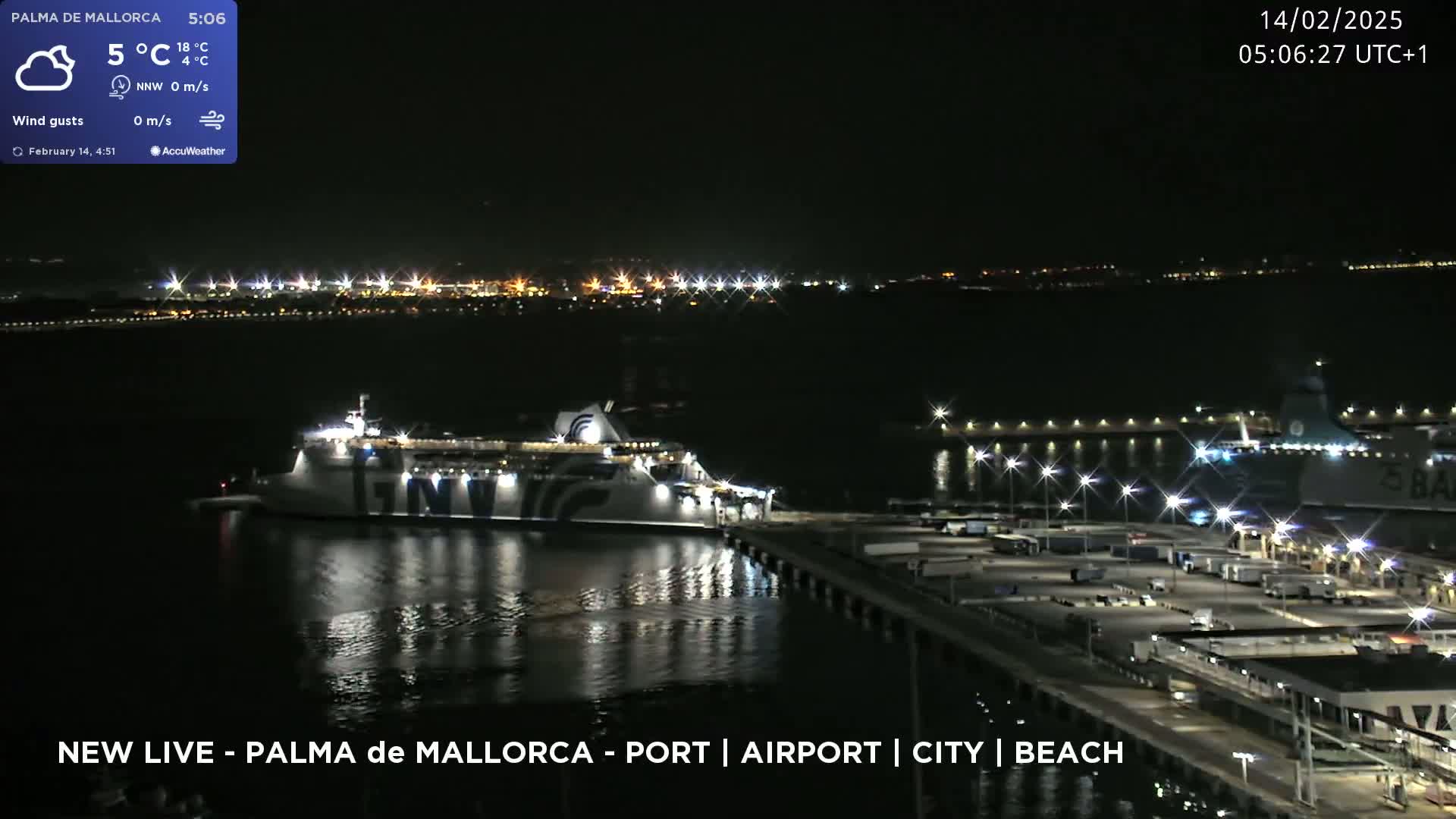A large ferry is docked at a port at night, with city lights visible in the distance under a clear sky.