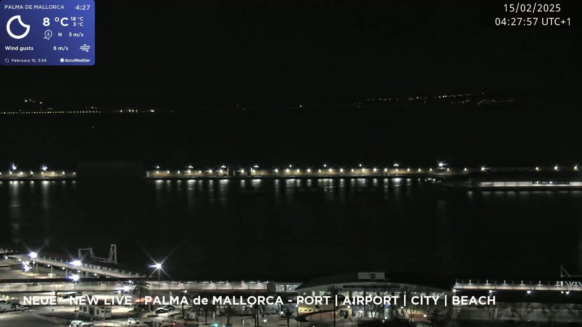 A nighttime view of a calm body of water with illuminated structures along the shoreline under a clear, dark sky.
