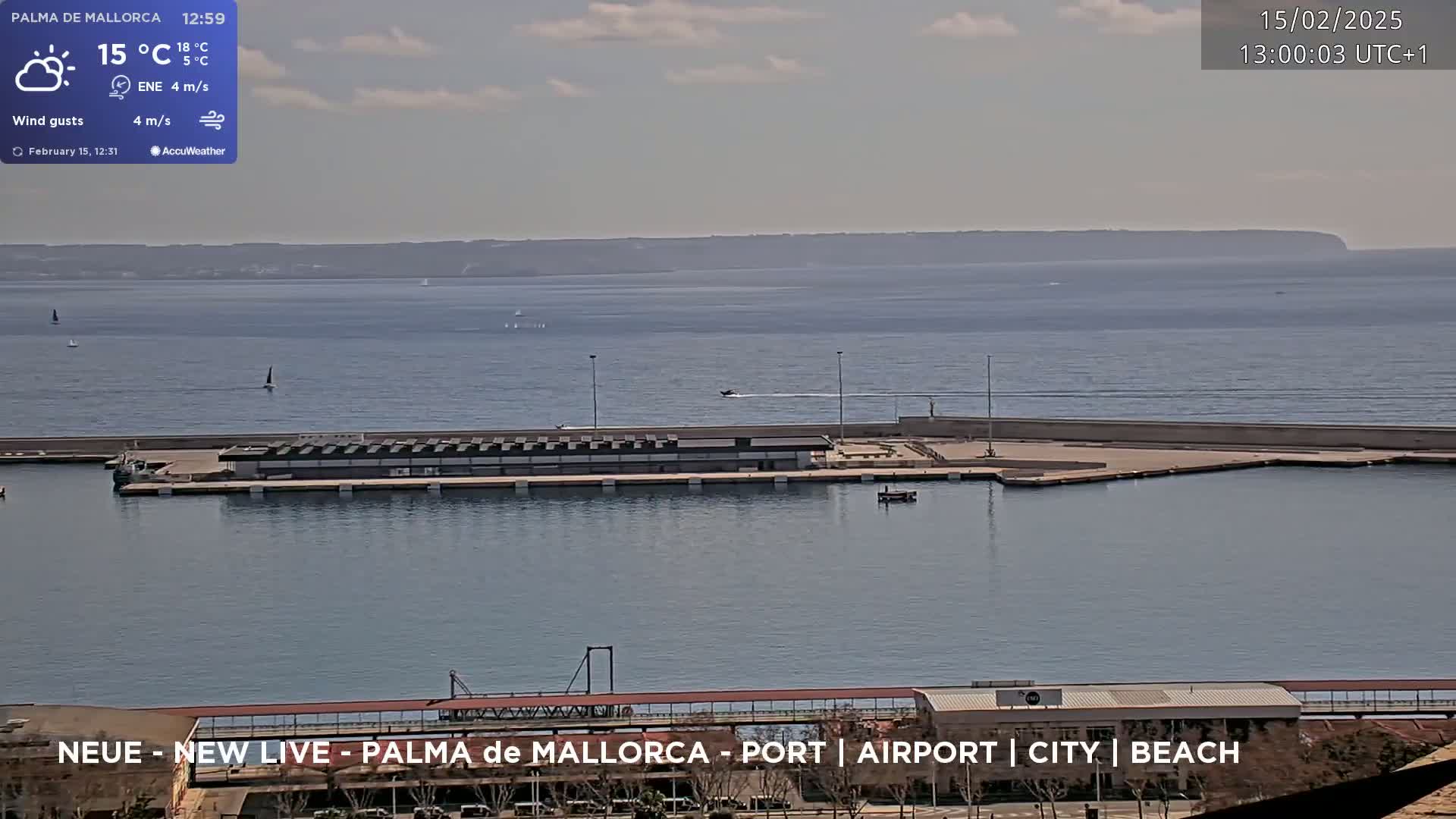 A partly sunny day shows a harbor with a long dock, several small boats, and a distant landmass across calm water.