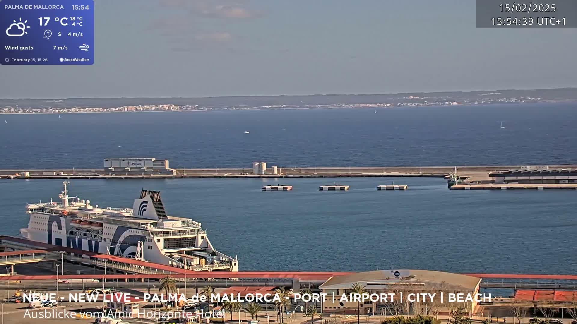 A ferry is docked at a port on a partly sunny day, with calm waters extending to a distant coastline.
