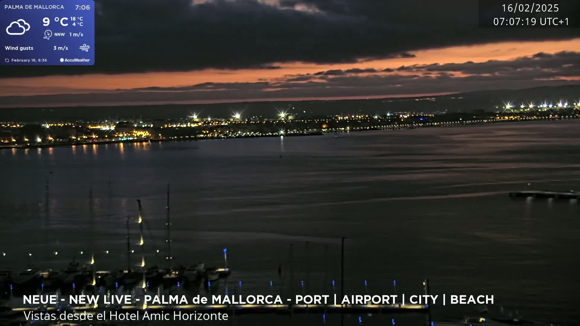 A nighttime view of a city across a body of water, under a mostly cloudy, dusky sky.