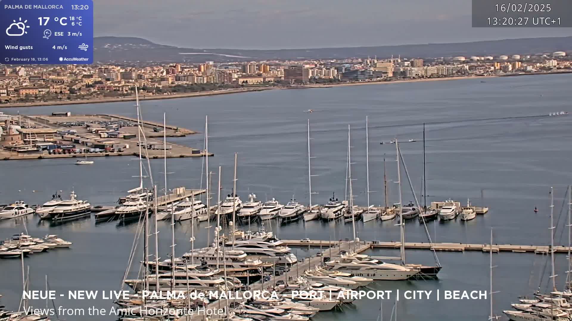A harbor filled with numerous yachts and sailboats is shown, with a city and calm bay visible in the background under a partly cloudy sky.