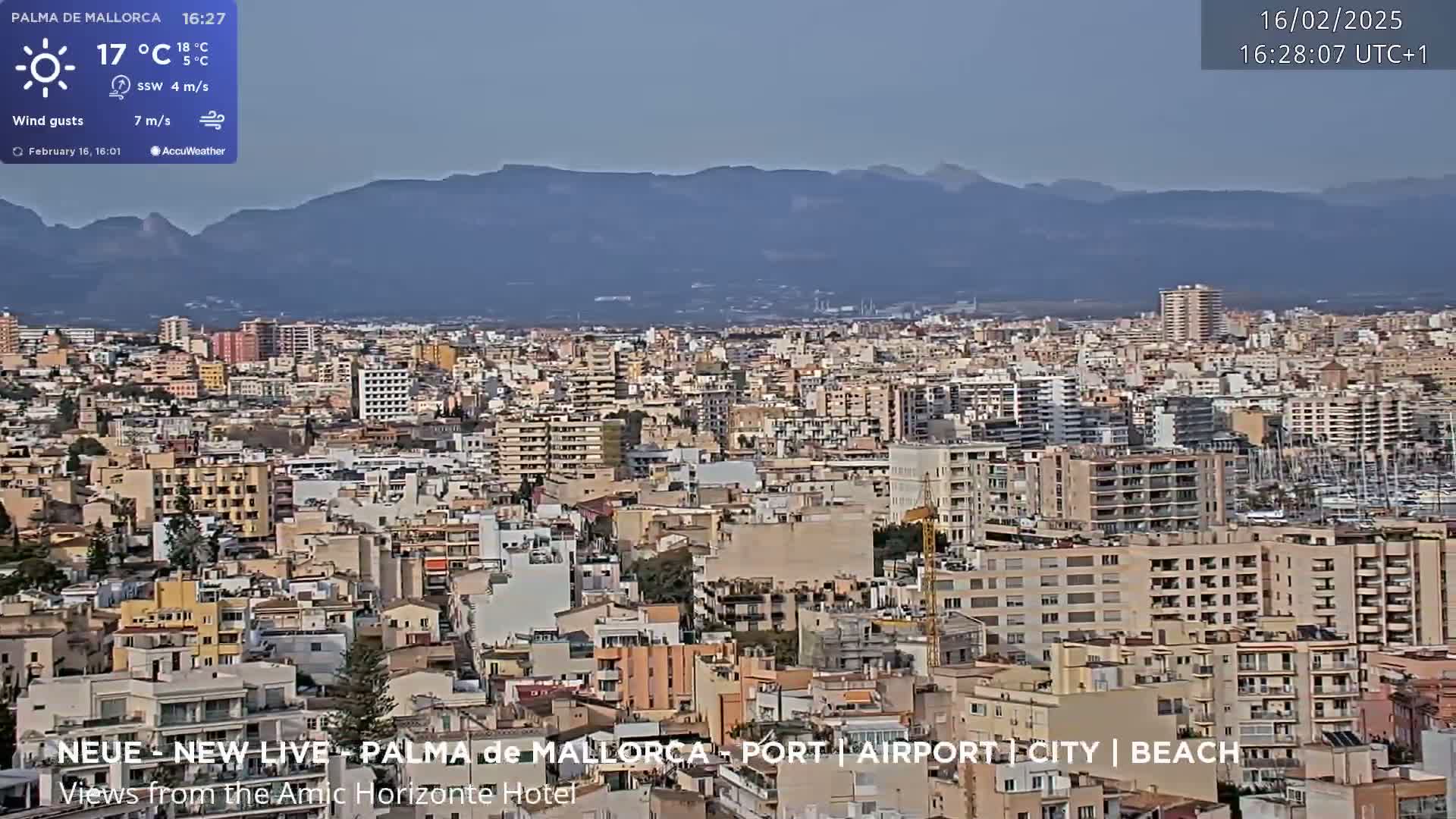 A sunny, clear day reveals a sprawling cityscape nestled against a backdrop of distant mountains.
