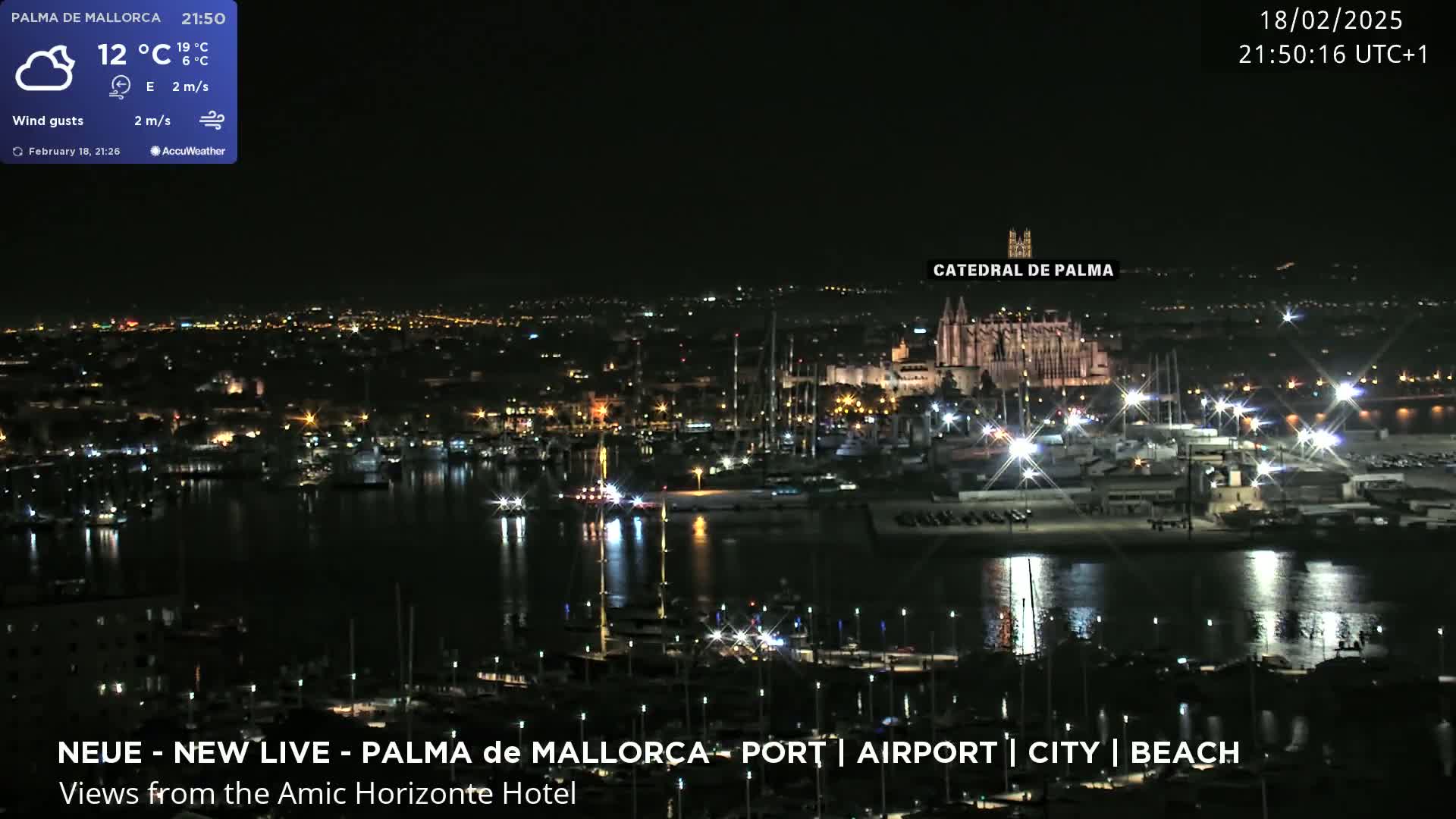 A nighttime view of a harbor and city, with a large cathedral illuminated, under partly cloudy skies.