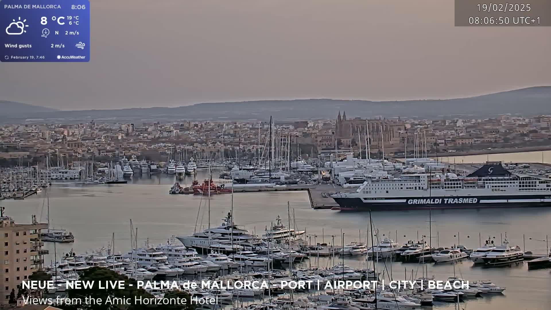A harbor filled with numerous yachts and a large ferry is shown under a hazy, light sky.