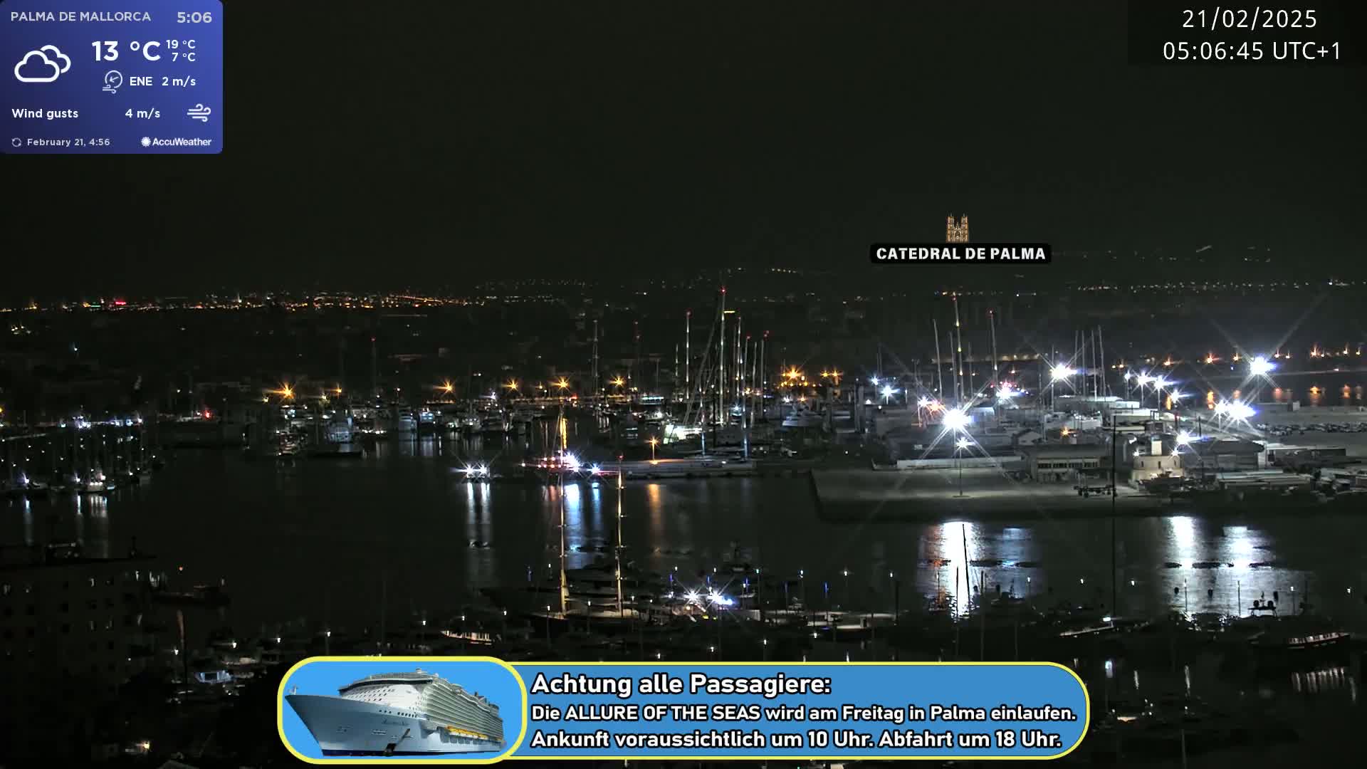 A nighttime harbor scene shows many boats and ships docked, with city lights in the background under partly cloudy skies.