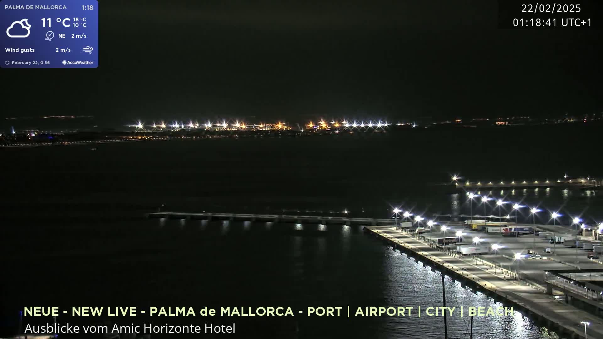 A nighttime, aerial view of a brightly lit port and city across a dark body of water under a clear sky.
