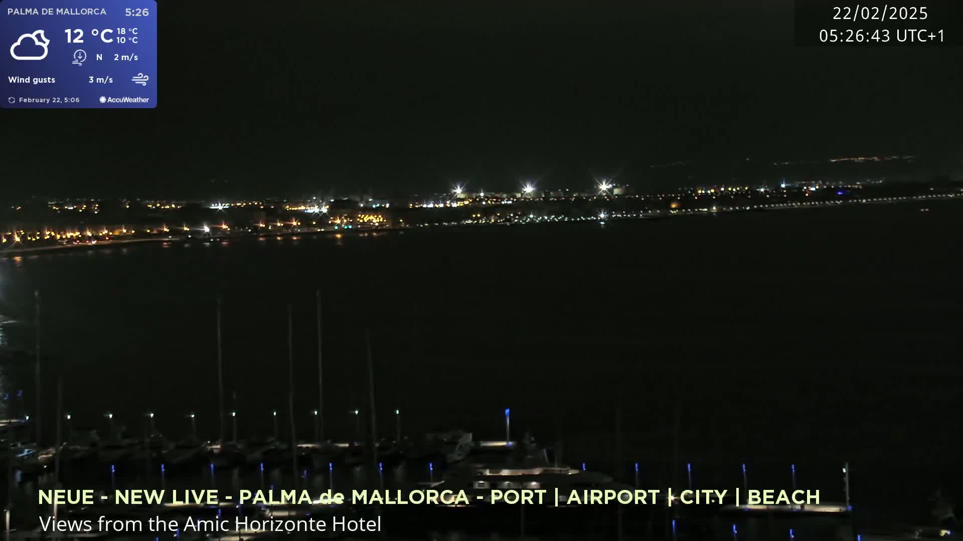 A nighttime view across a dark body of water shows a distant city skyline illuminated with lights, and a closer foreground of moored boats.