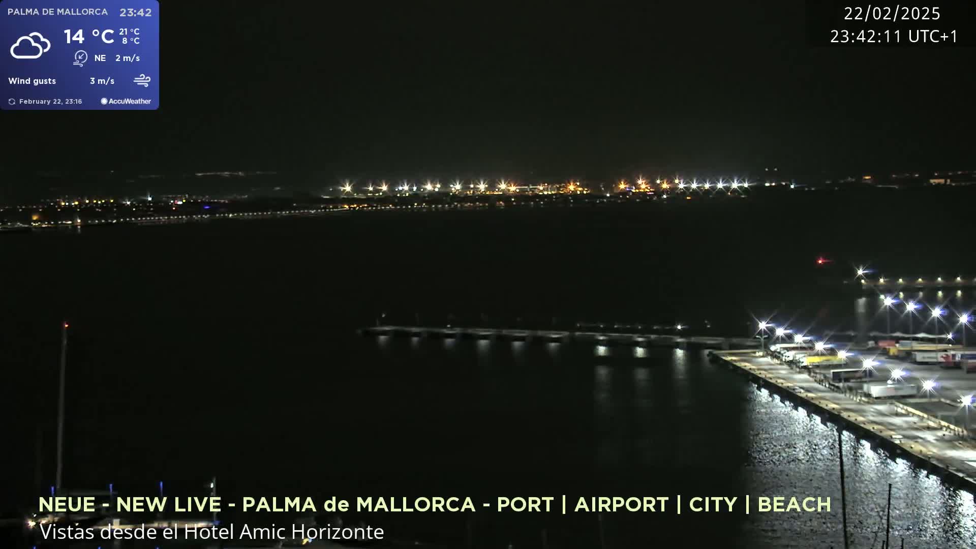 A nighttime view of a city's illuminated port and waterfront, with a calm body of water reflecting the lights.