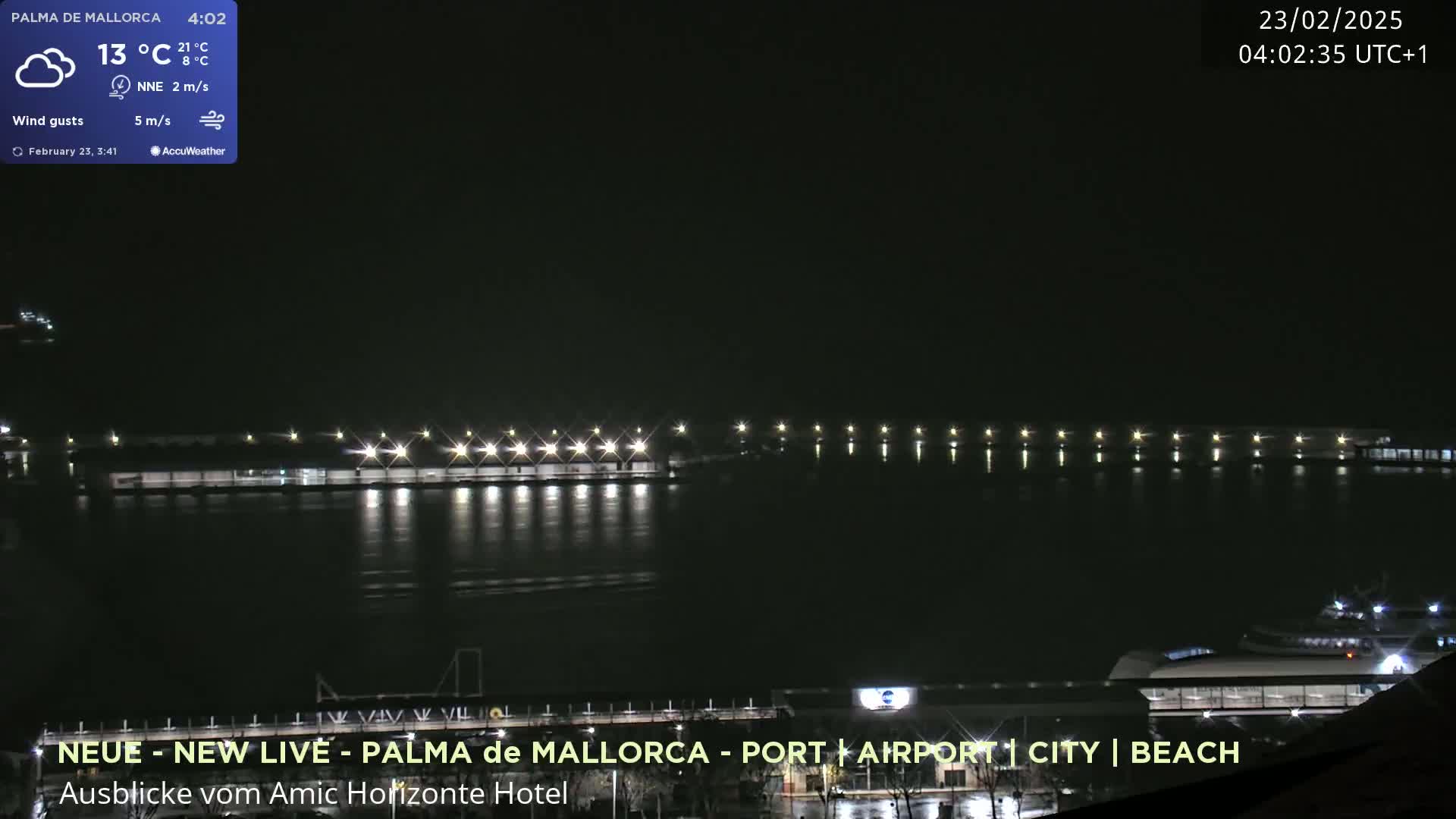 A nighttime view of a calm body of water with a long pier lit by many lights, and a docked boat visible near a building.