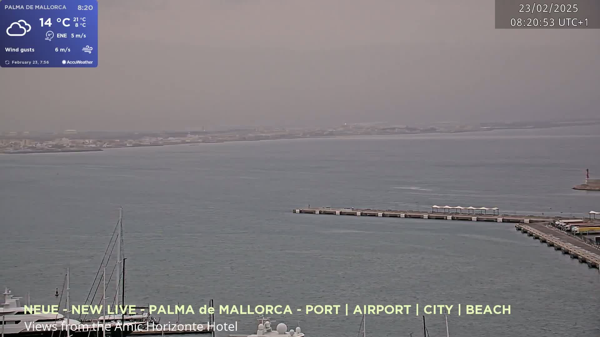 A hazy view of a harbor with a city in the distance and several boats docked, under a somewhat overcast sky.