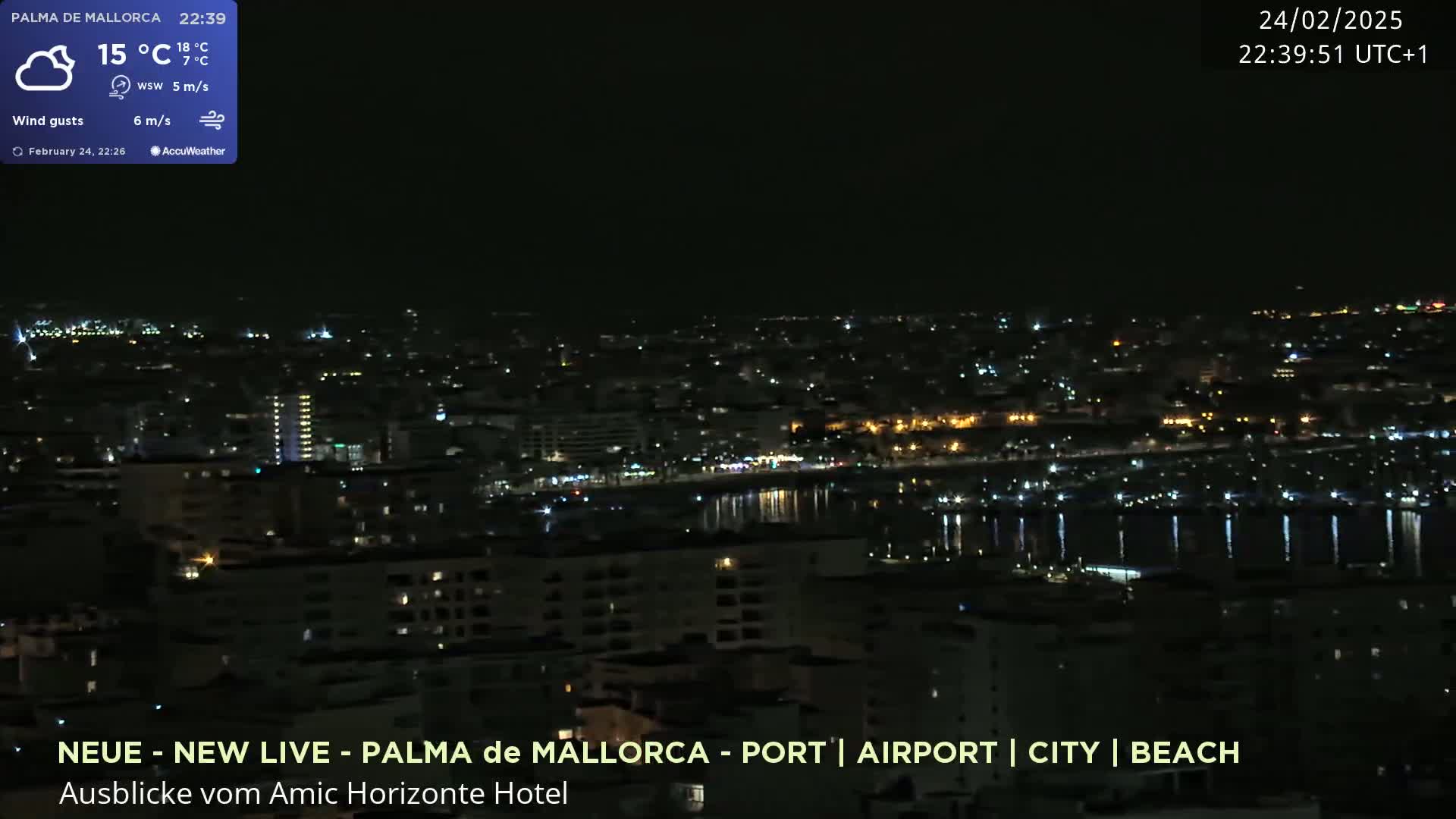 A nighttime view of a city illuminated by lights, with a calm body of water reflecting the city lights under a clear sky.