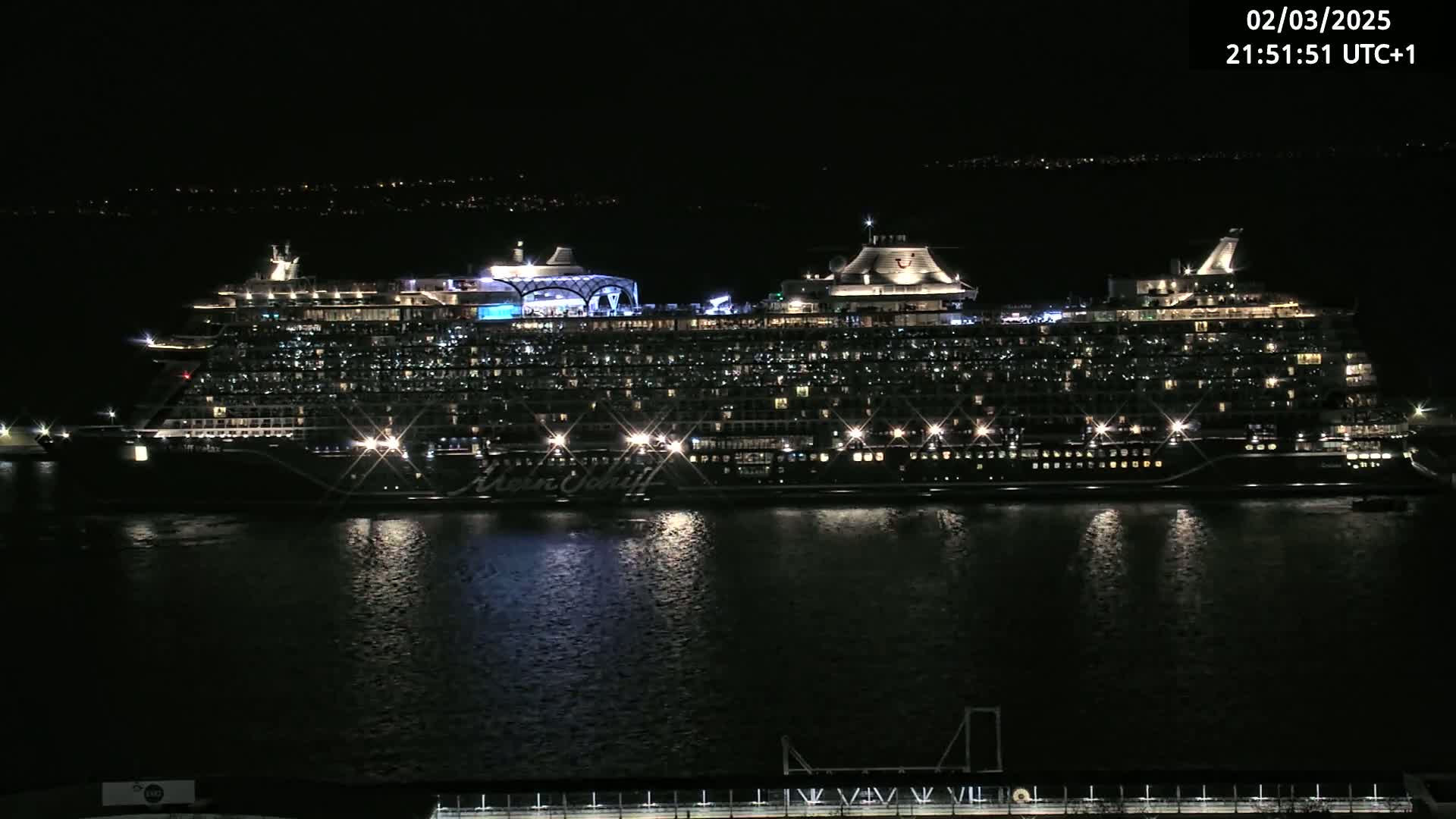 A large, brightly lit cruise ship is docked at night on calm water.