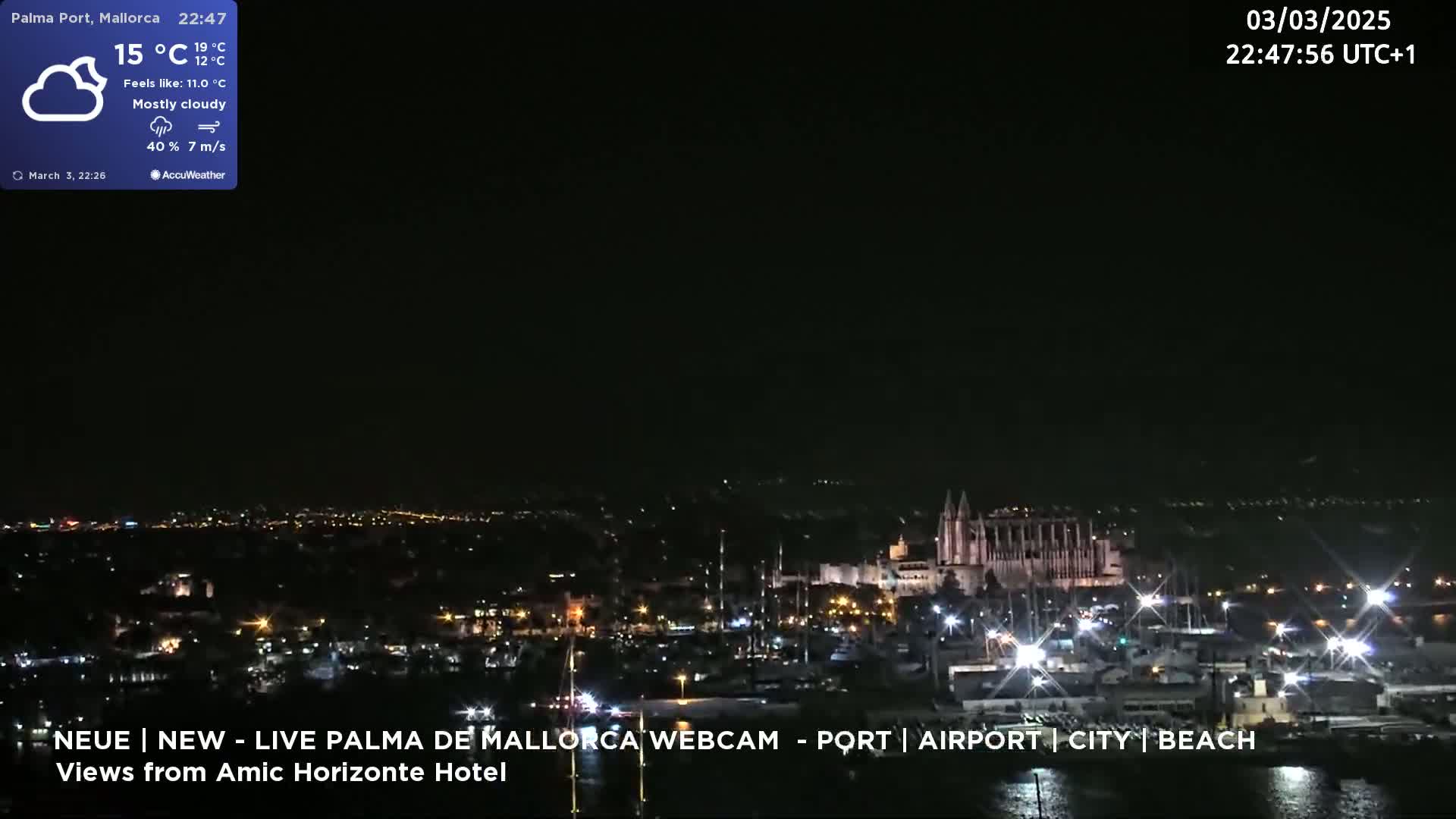 A mostly cloudy night scene shows a brightly lit city harbor with a large cathedral in the background.