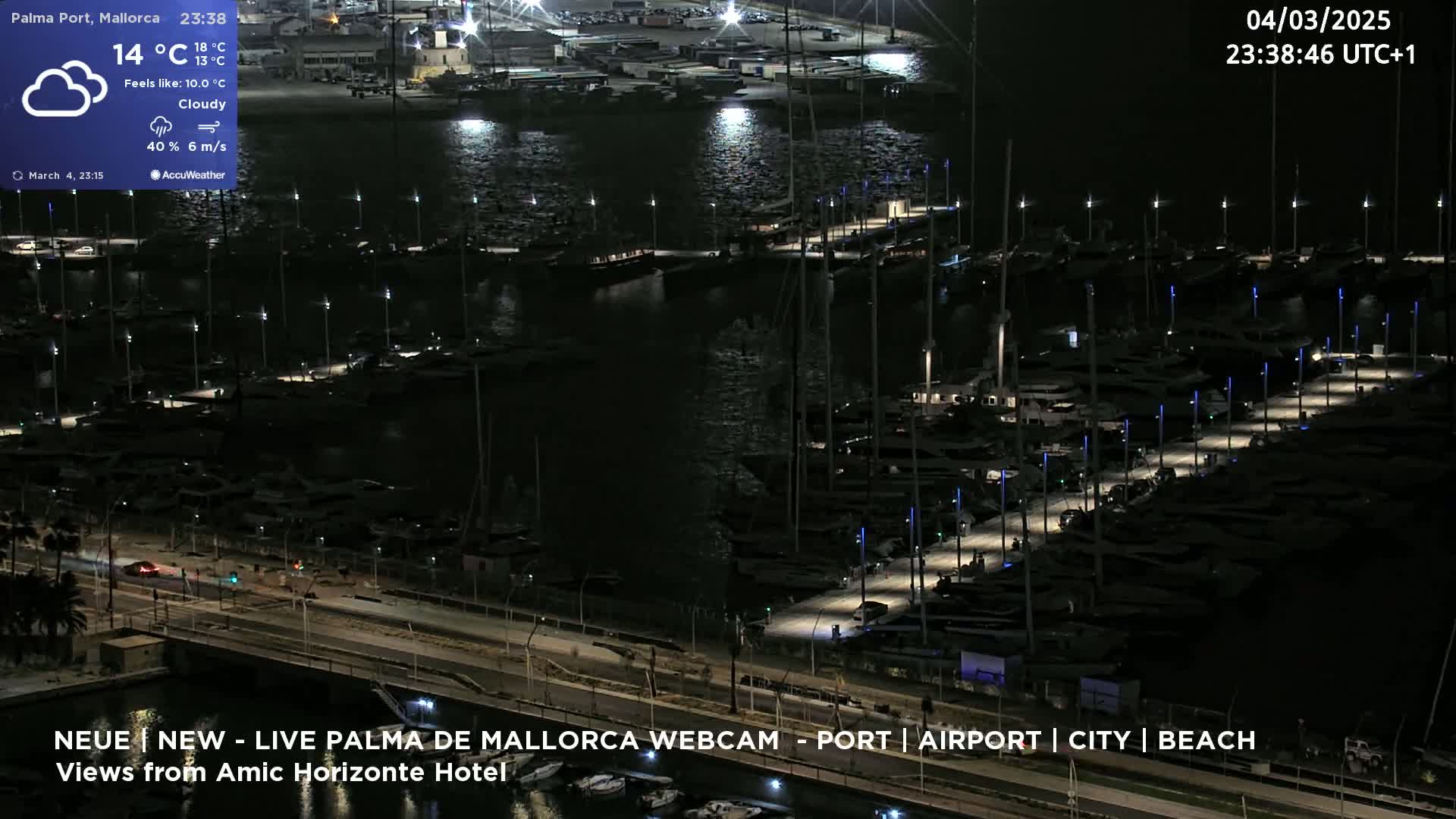 A nighttime, cloudy view of a marina filled with many boats, illuminated by lights, with a road and some cars visible alongside.