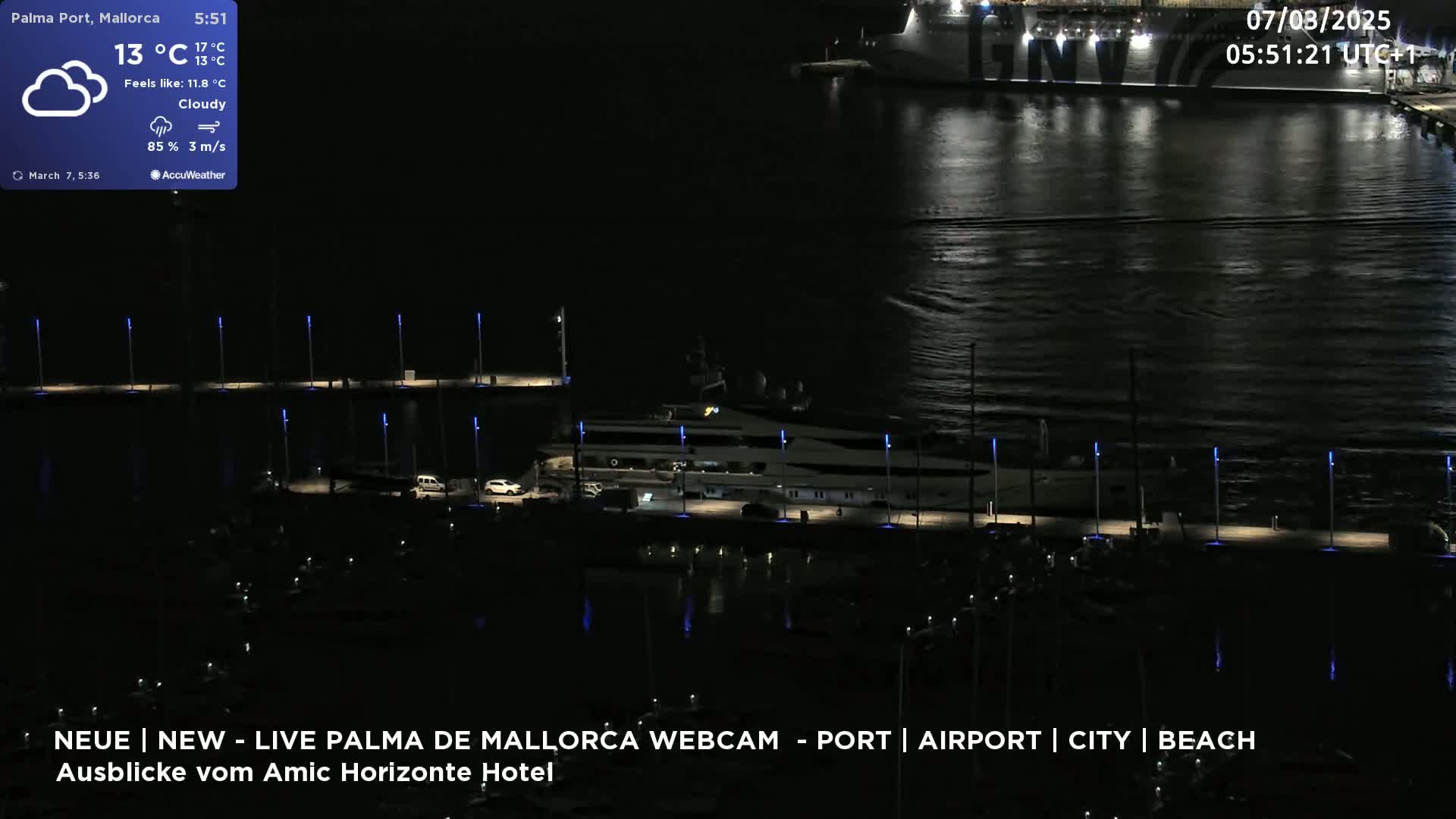 A nighttime harbor scene shows a large yacht docked near a pier, with a larger ship visible in the distance under a cloudy sky.