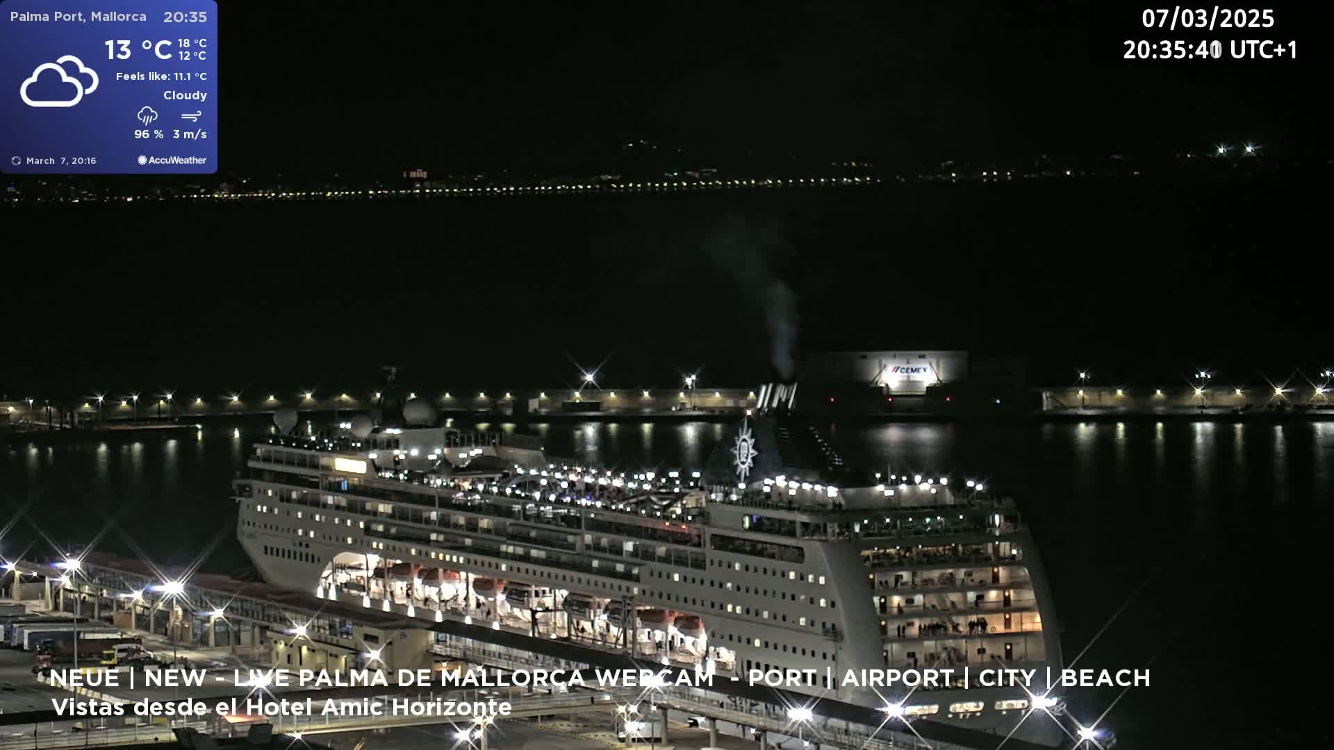 A large cruise ship is docked at a port at night under cloudy skies.