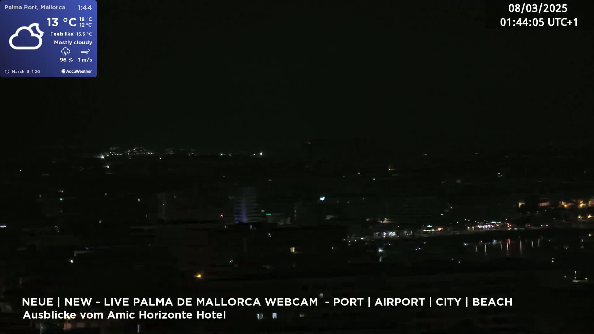 A nighttime, mostly cloudy view of a city illuminated by scattered lights, near a body of water.