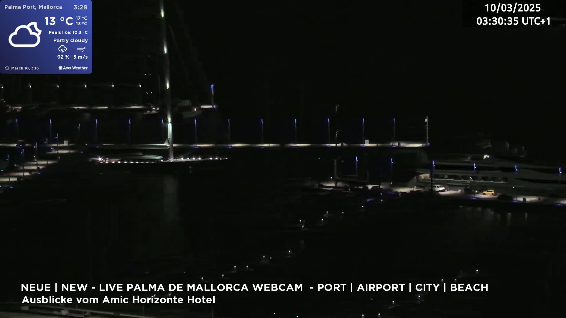 A nighttime view of a marina with boats docked, illuminated by lights under partly cloudy skies.