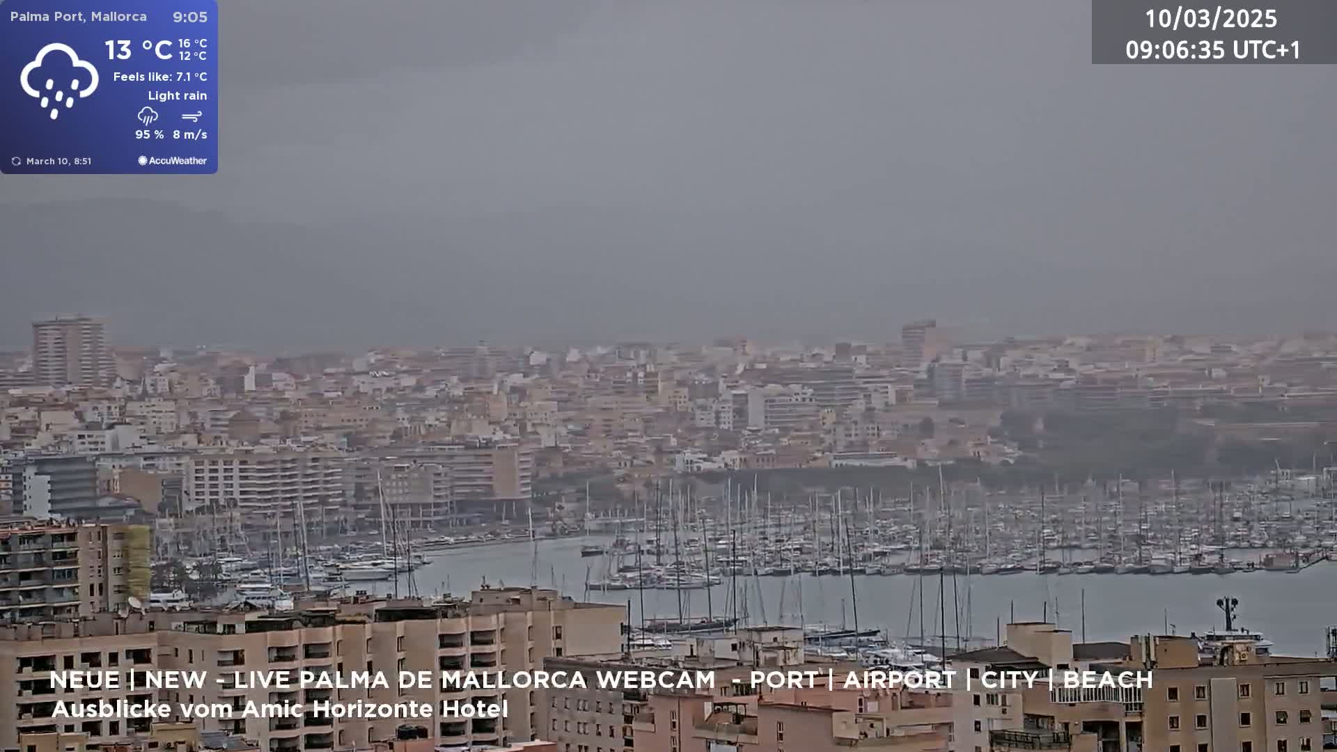 A hazy, light rain falls over a city harbor filled with numerous boats, with buildings extending into the distance under a gray sky.