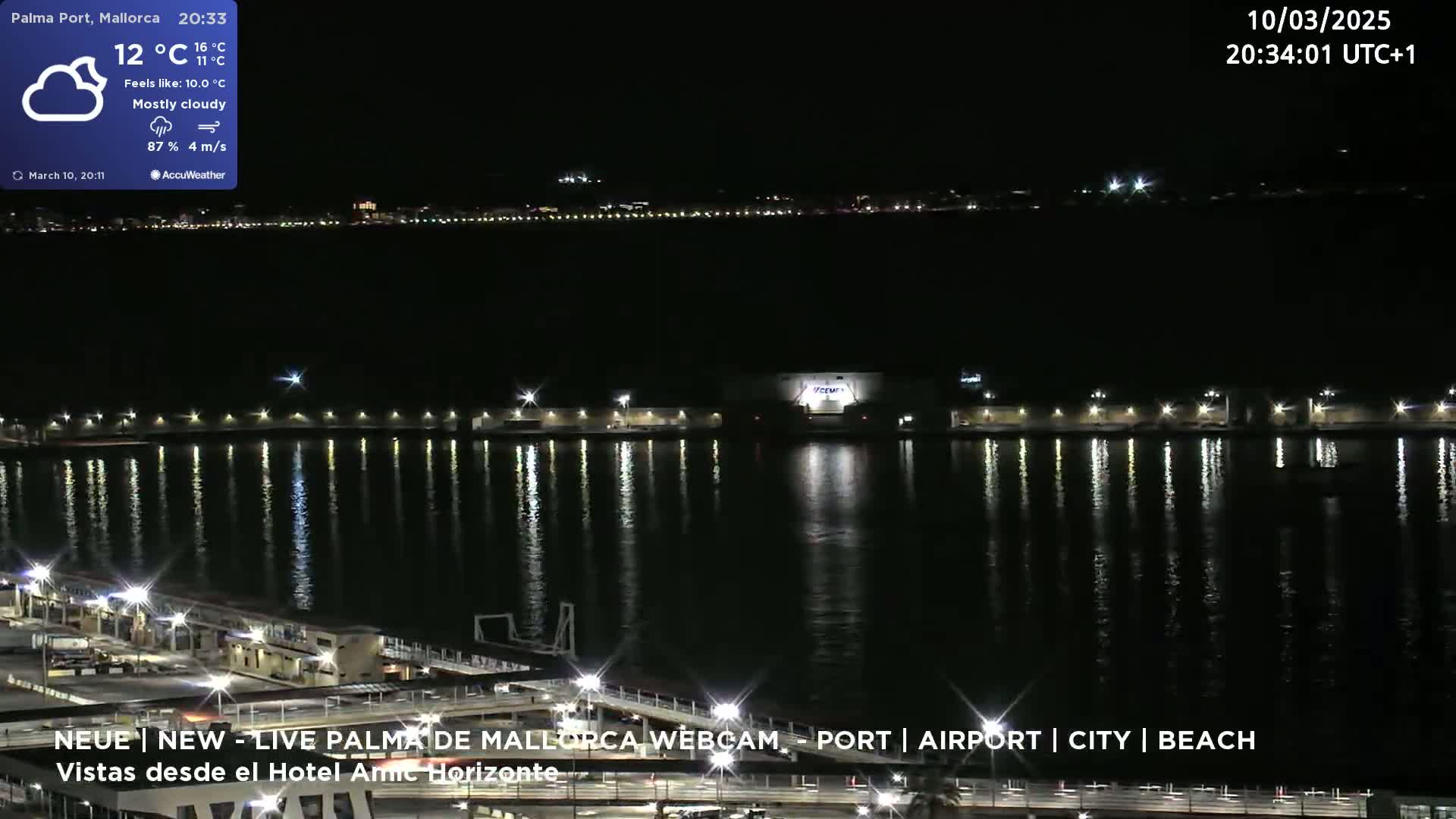 A mostly cloudy nighttime scene shows a harbor with lights reflecting on the water, and a city skyline in the distance.