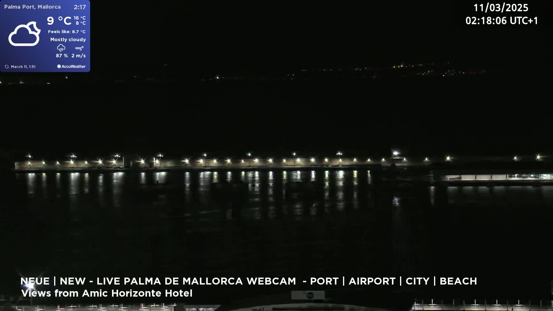 A nighttime view of a waterfront area with lights illuminating a dark body of water and a long, low structure.