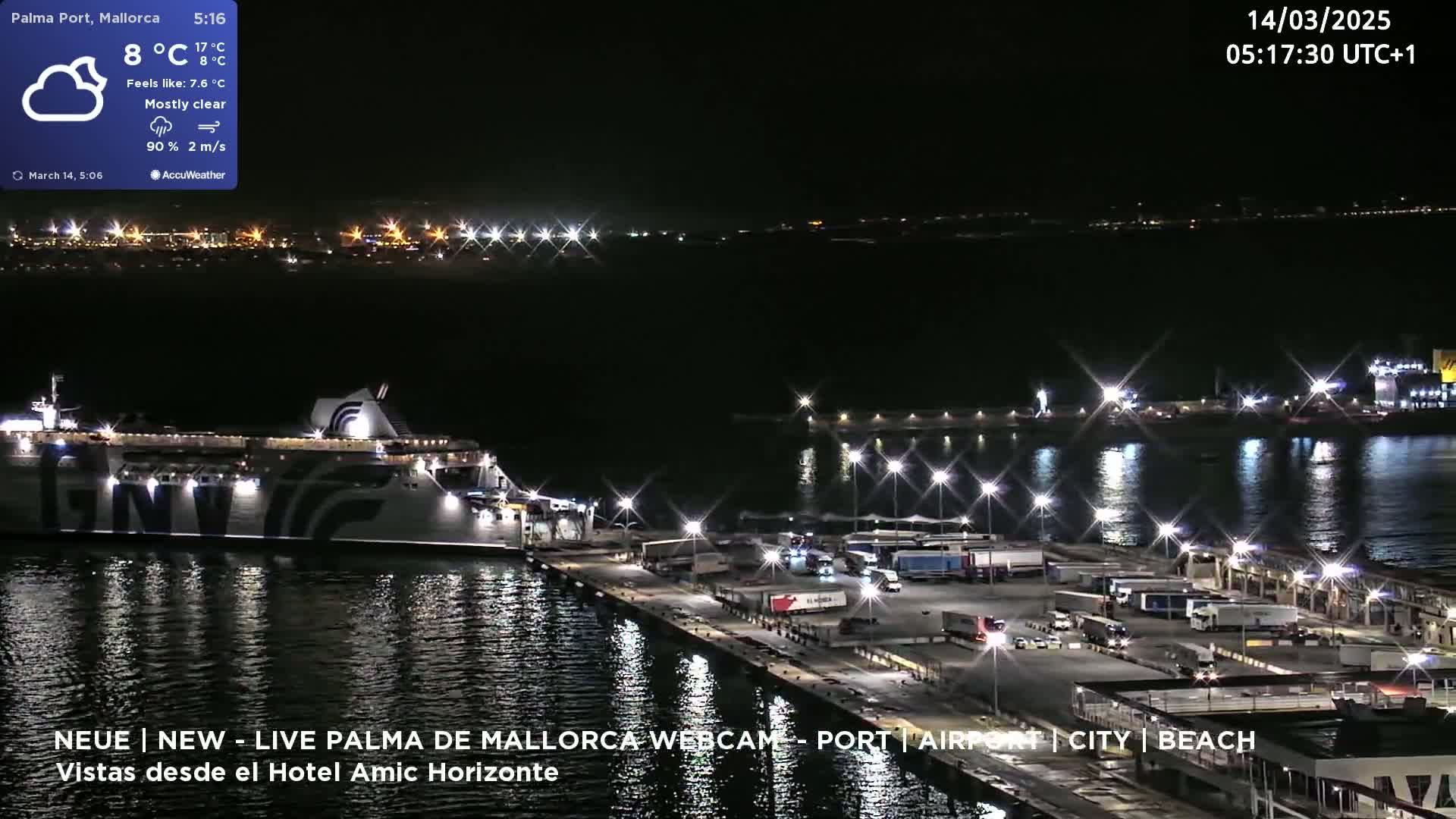 A large ferry is docked at a brightly lit port at night under mostly clear skies.
