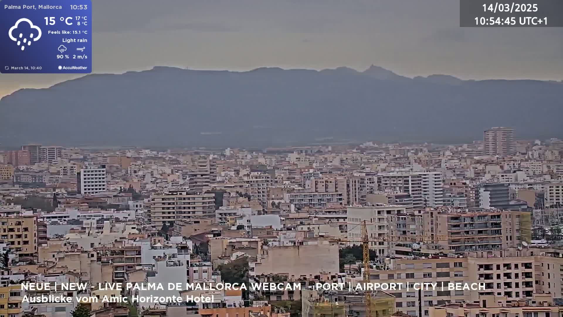 A sprawling city with light rain and overcast skies, nestled beneath a range of distant mountains.