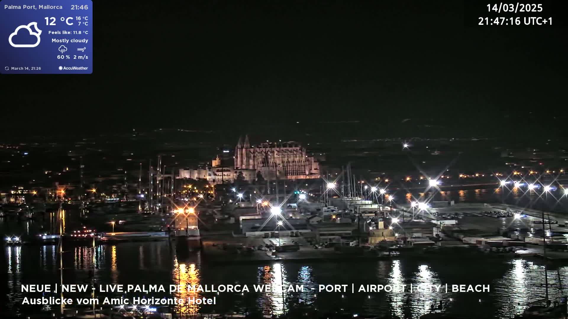 A nighttime, mostly cloudy view of a harbor with a large illuminated building in the background, and many lights reflecting on the water.