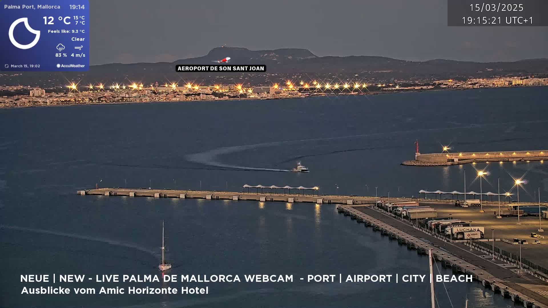 A nighttime aerial view of a harbor with a city and airport in the distance under clear skies.