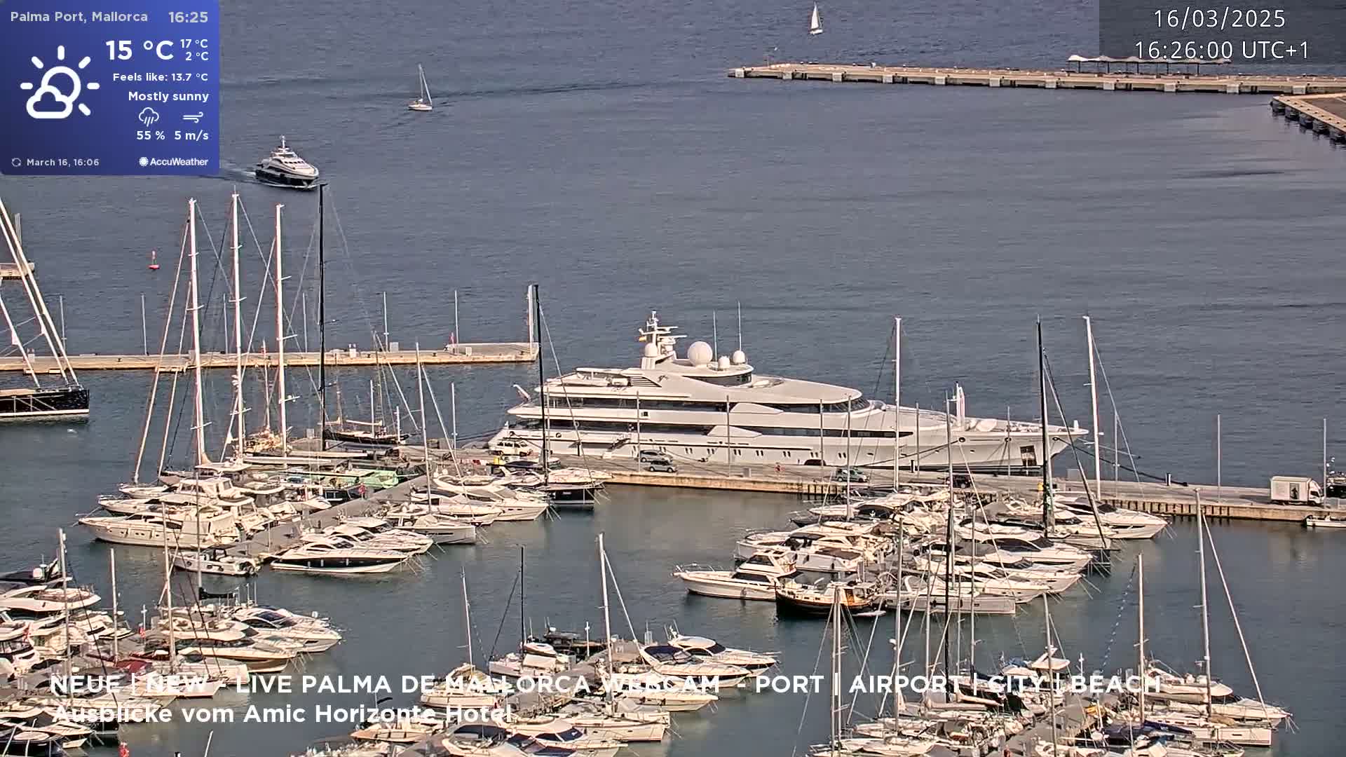 A large yacht is docked in a marina filled with numerous smaller boats under mostly sunny skies.