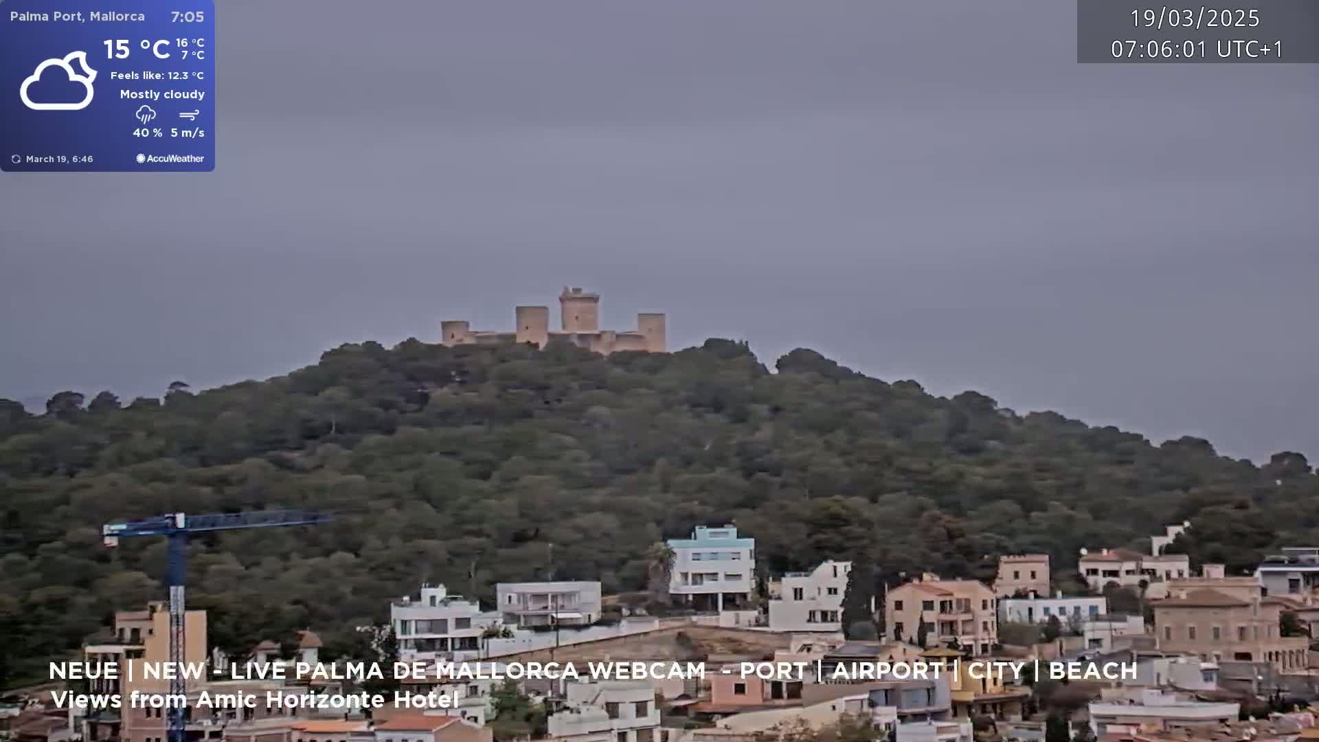 A mostly cloudy scene shows a hilltop castle overlooking a town with houses and a construction crane, under a grey sky.